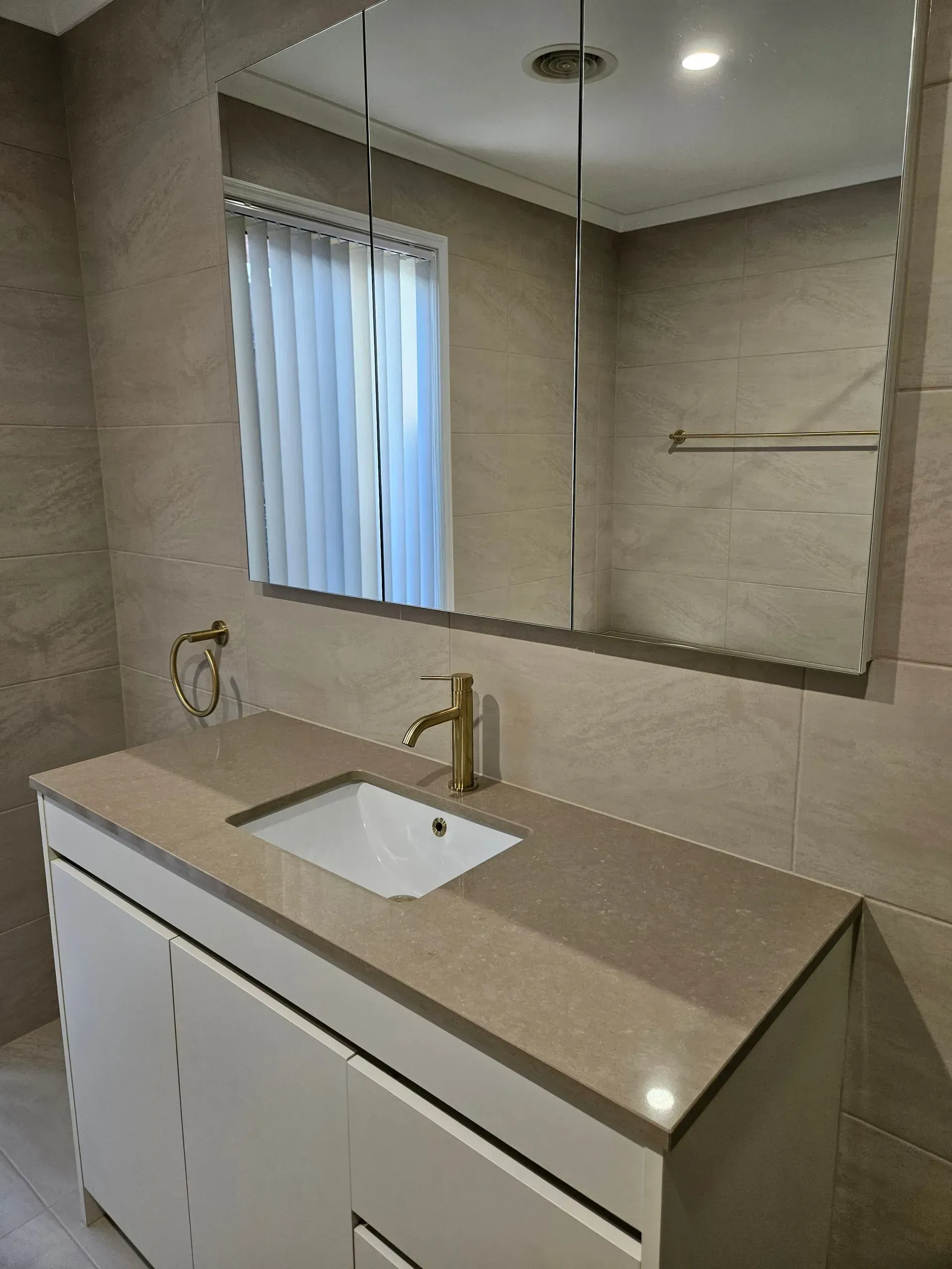 Modern bathroom vanity with beige countertop, white cabinets, mirror, and brass faucet under recessed lighting