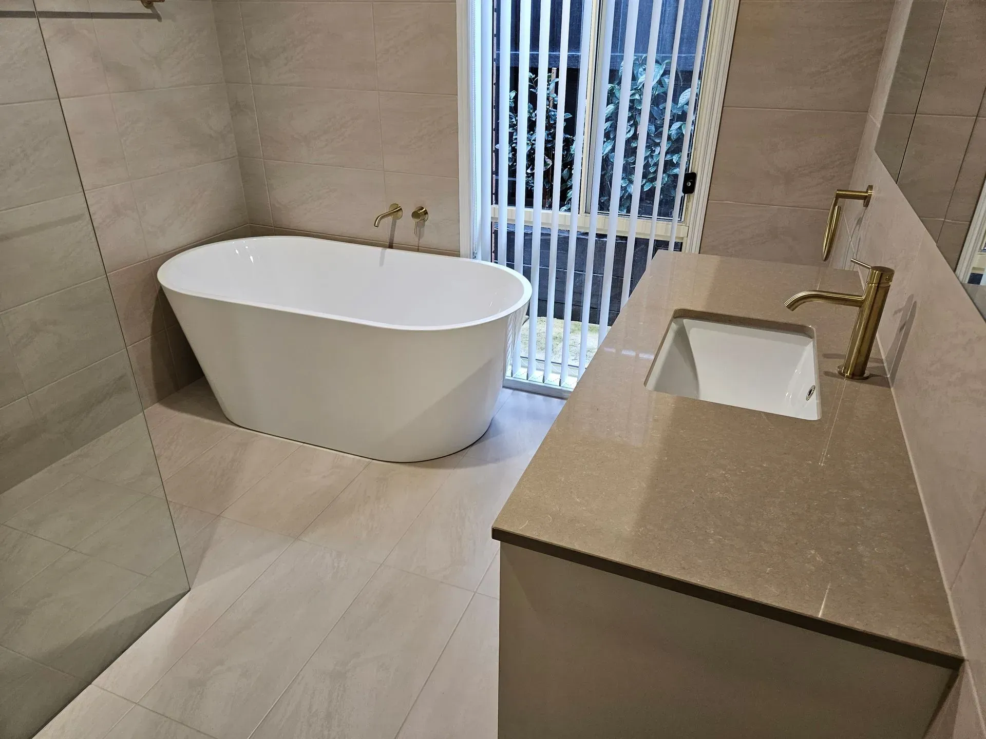 Modern bathroom with freestanding tub, vanity sink, and striped window blinds