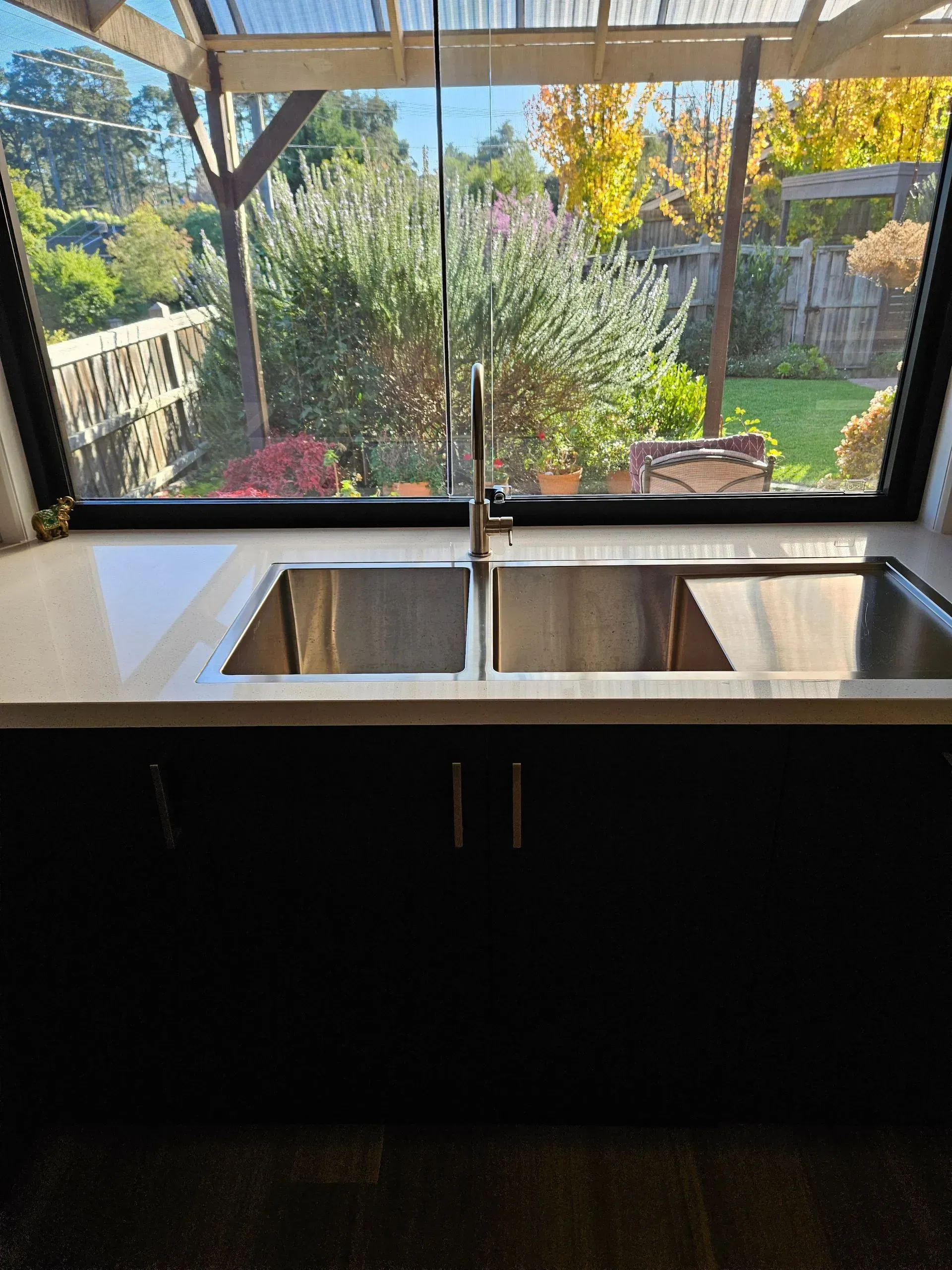 Modern kitchen sink beneath a window overlooking a sunny backyard garden