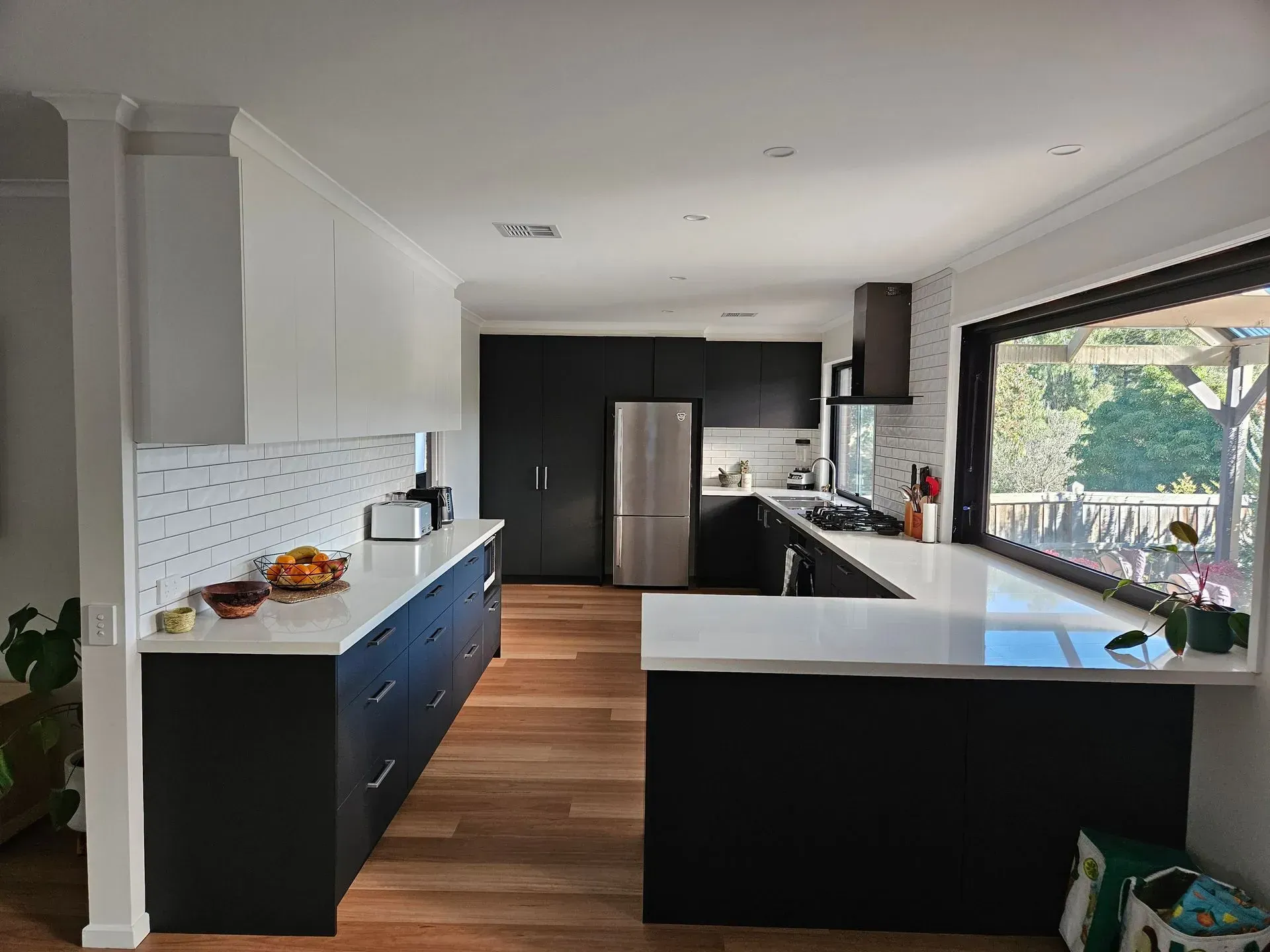 Modern kitchen with dark cabinets, white counters, wood floors, and a large window above the sink