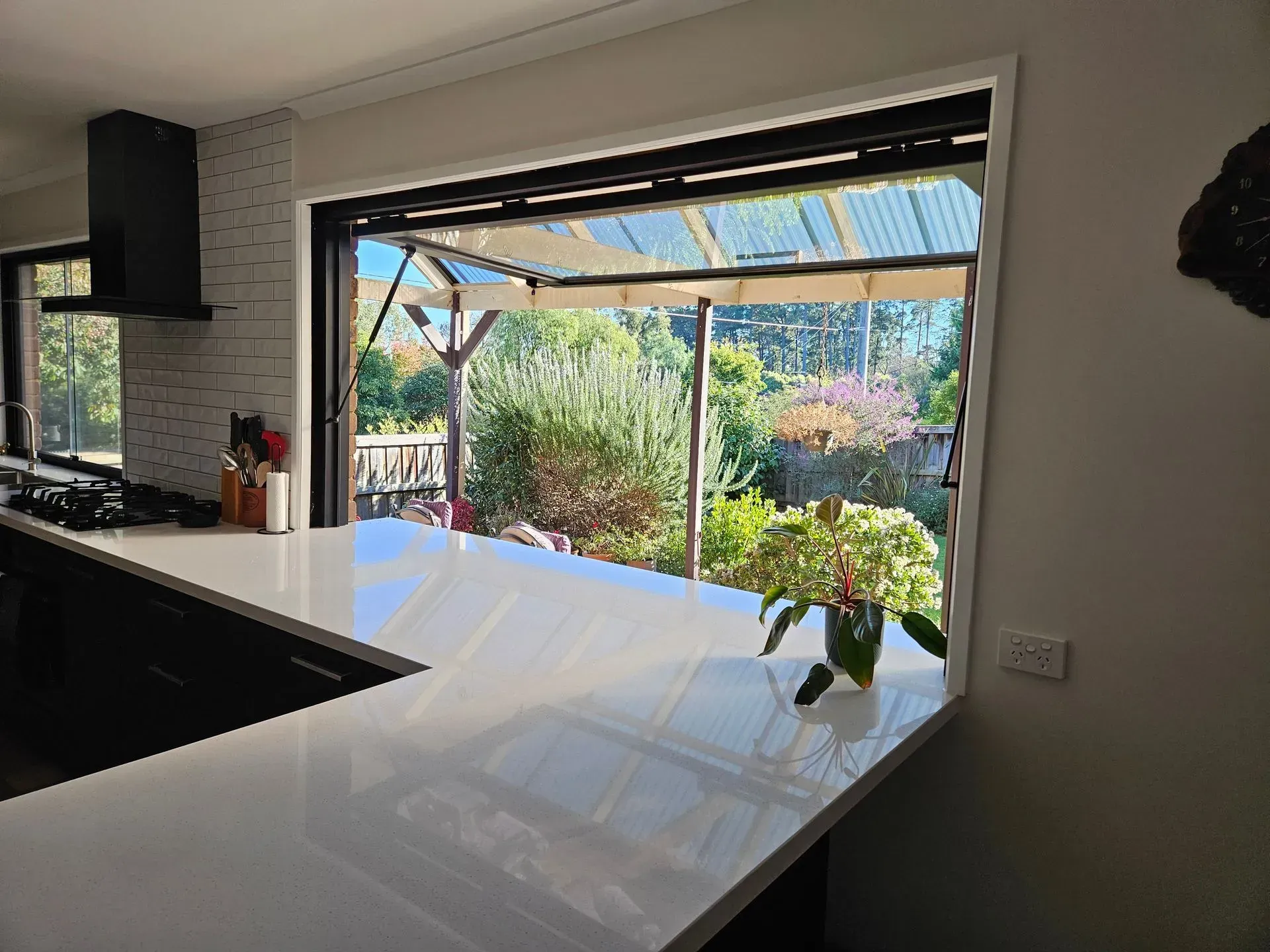 Modern kitchen with a large open window looking out to a sunny garden and patio.
