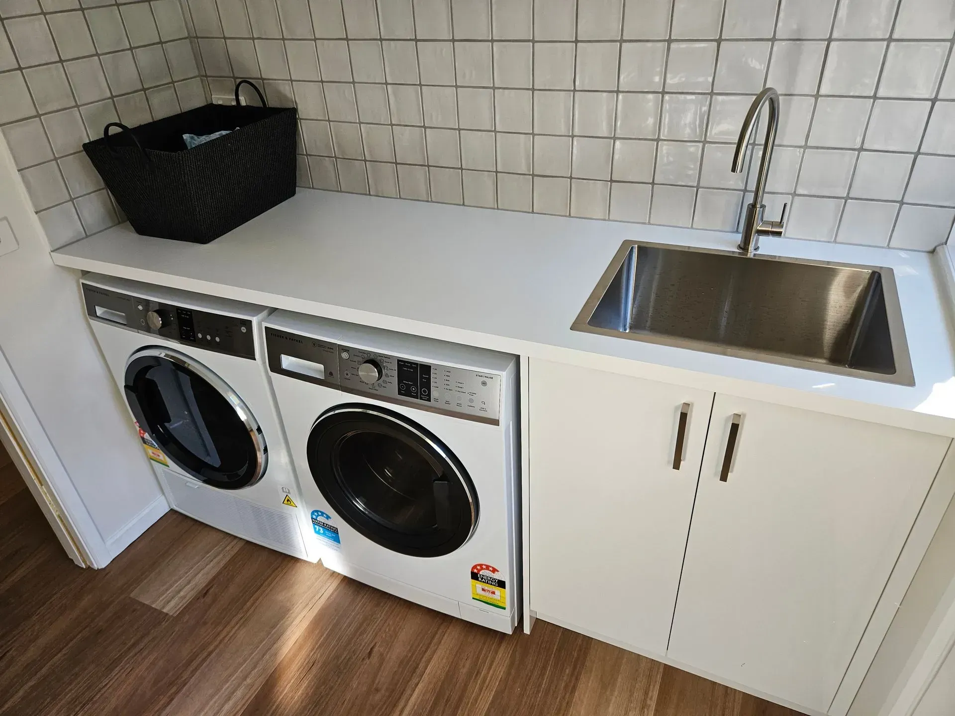 Laundry room with washer and dryer under a white countertop beside a stainless steel sink and cabinet.