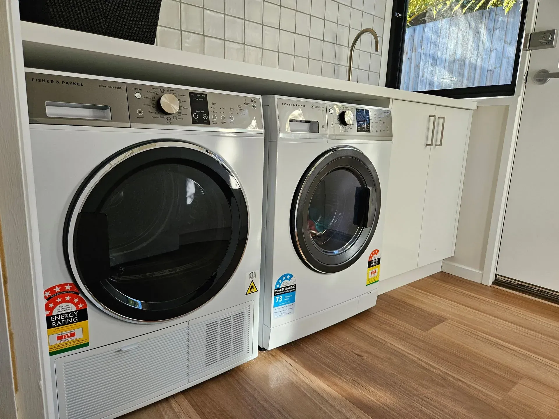 Two front-loading laundry machines in a bright utility room with white cabinets and wood flooring