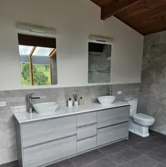 Modern bathroom with double vanity, twin sinks, toilet, gray tile, and wood ceiling