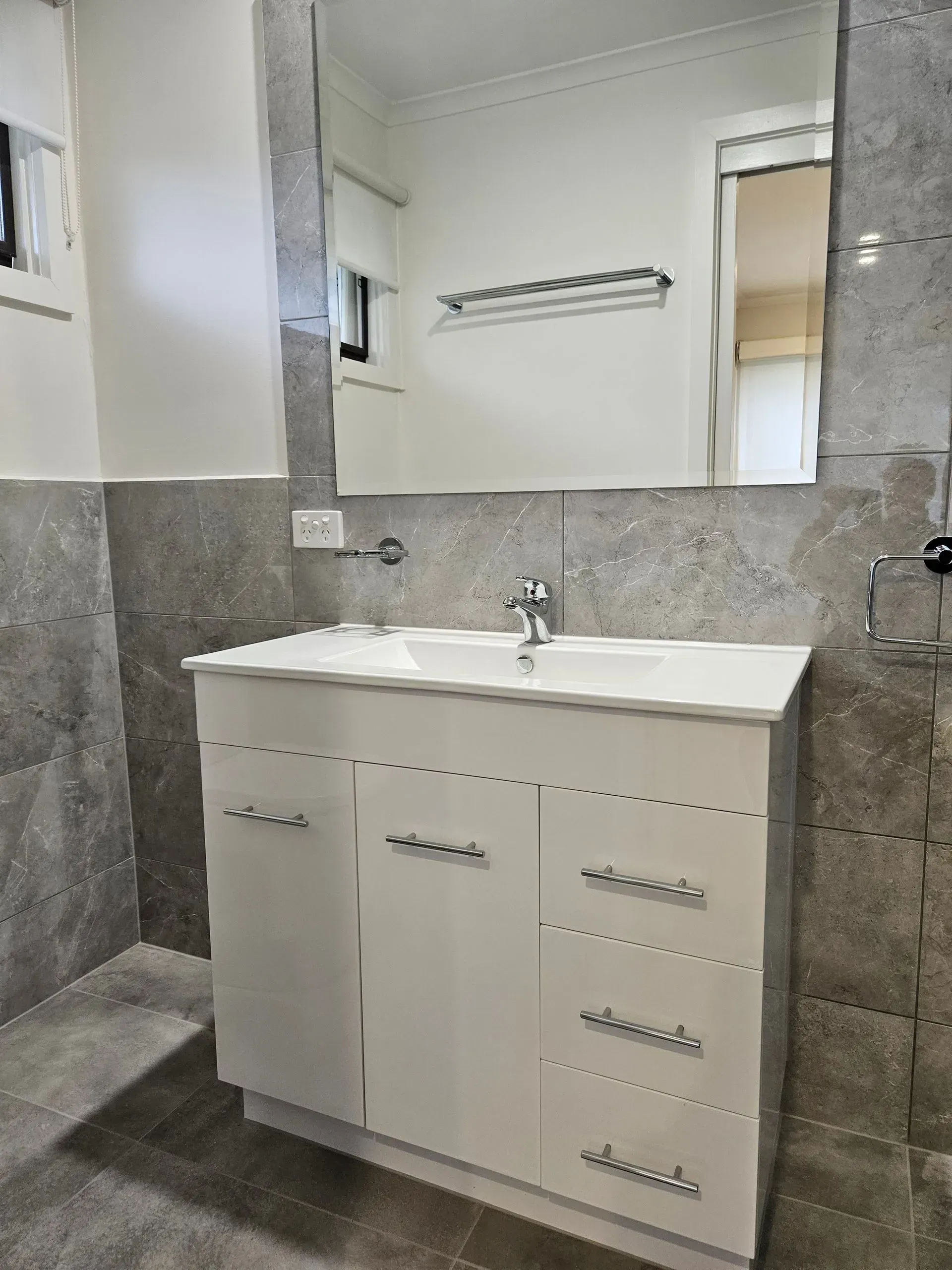 White bathroom vanity with sink, mirror, and gray tiled walls in a small bathroom
