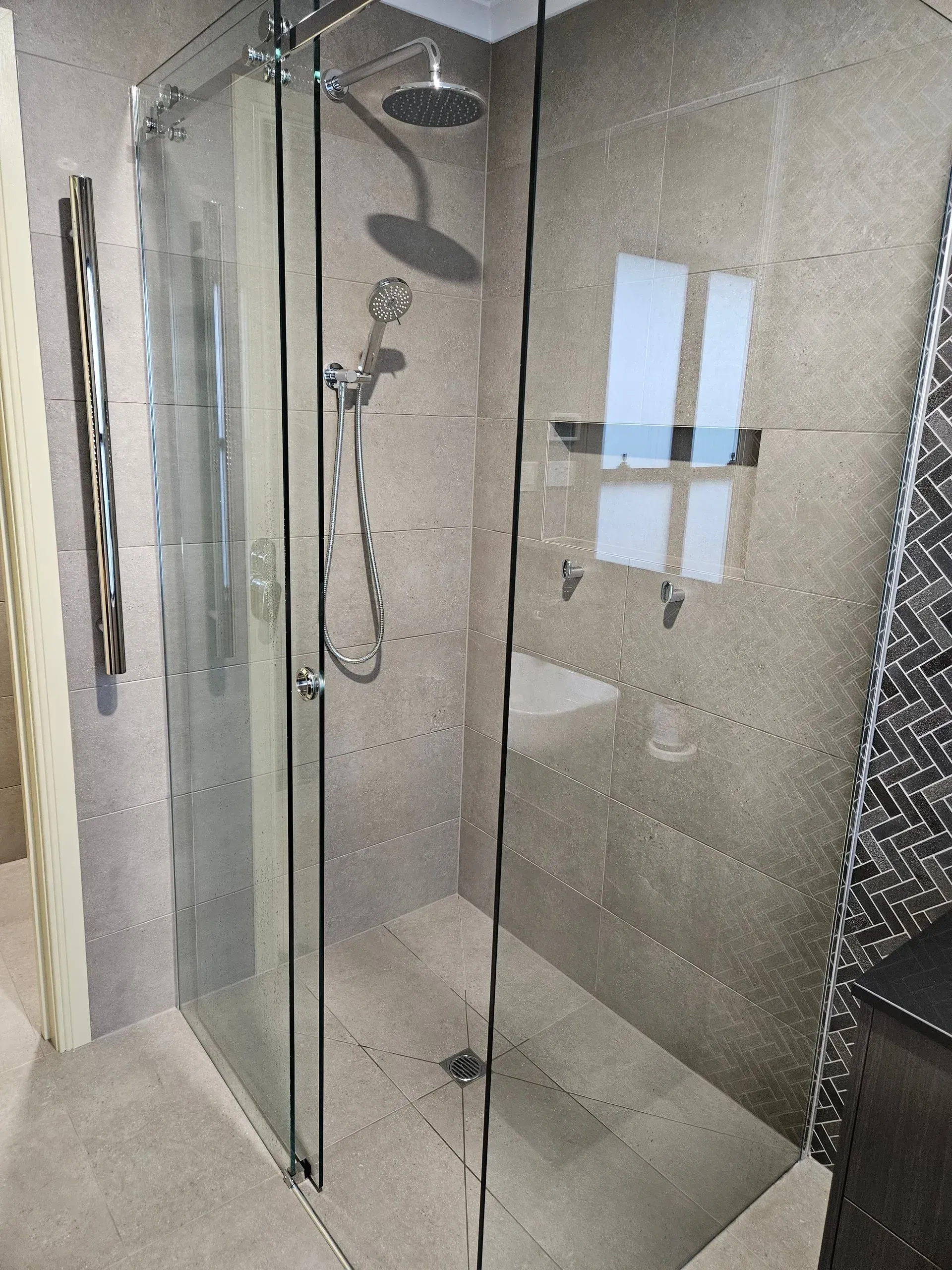 Modern glass shower stall with chrome fixtures and beige tile walls