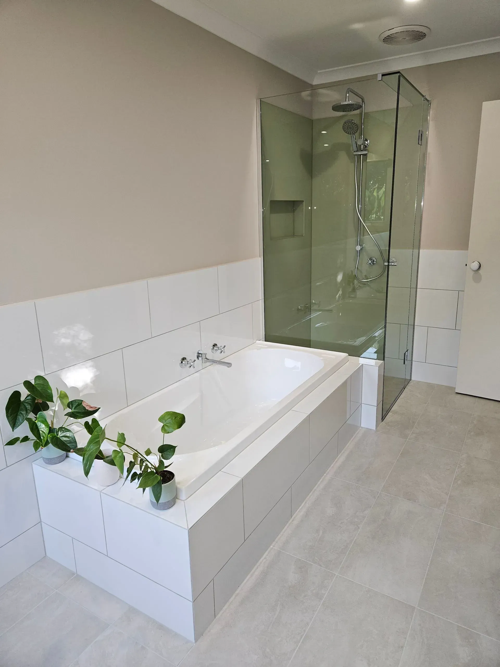 Modern bathroom with white bathtub, glass shower enclosure, and green vine decor on the tub edge