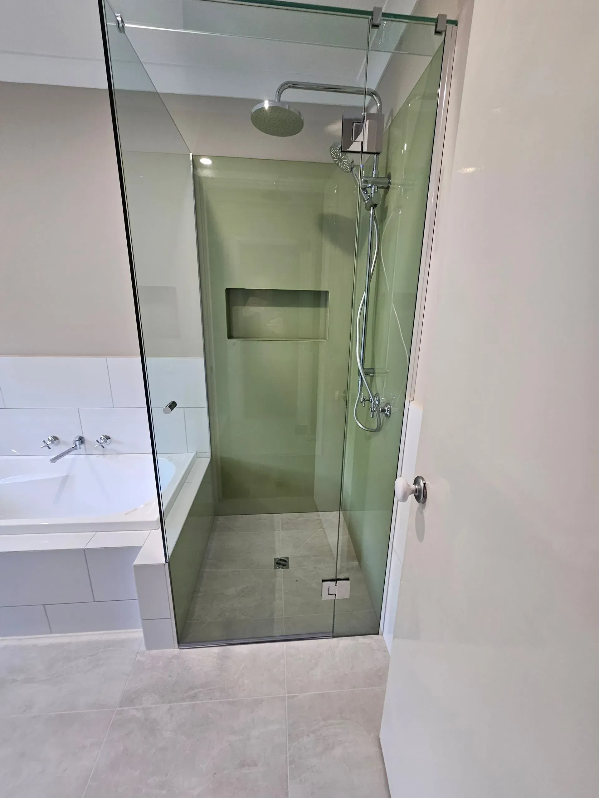 Bathroom with glass-enclosed walk-in shower, white tile, and handheld showerhead.