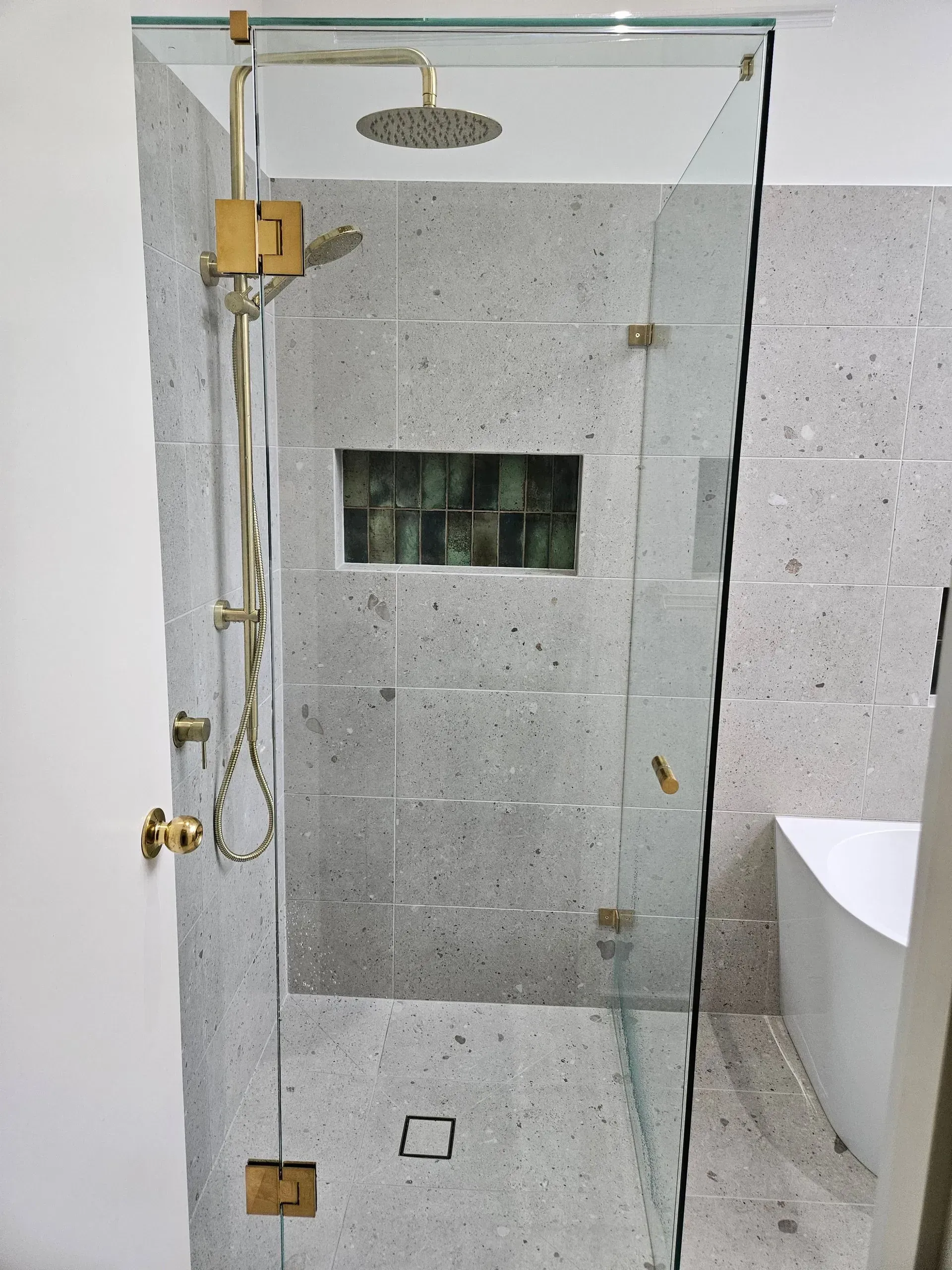 Glass shower enclosure with brass fixtures, handheld shower, and gray stone-tile walls