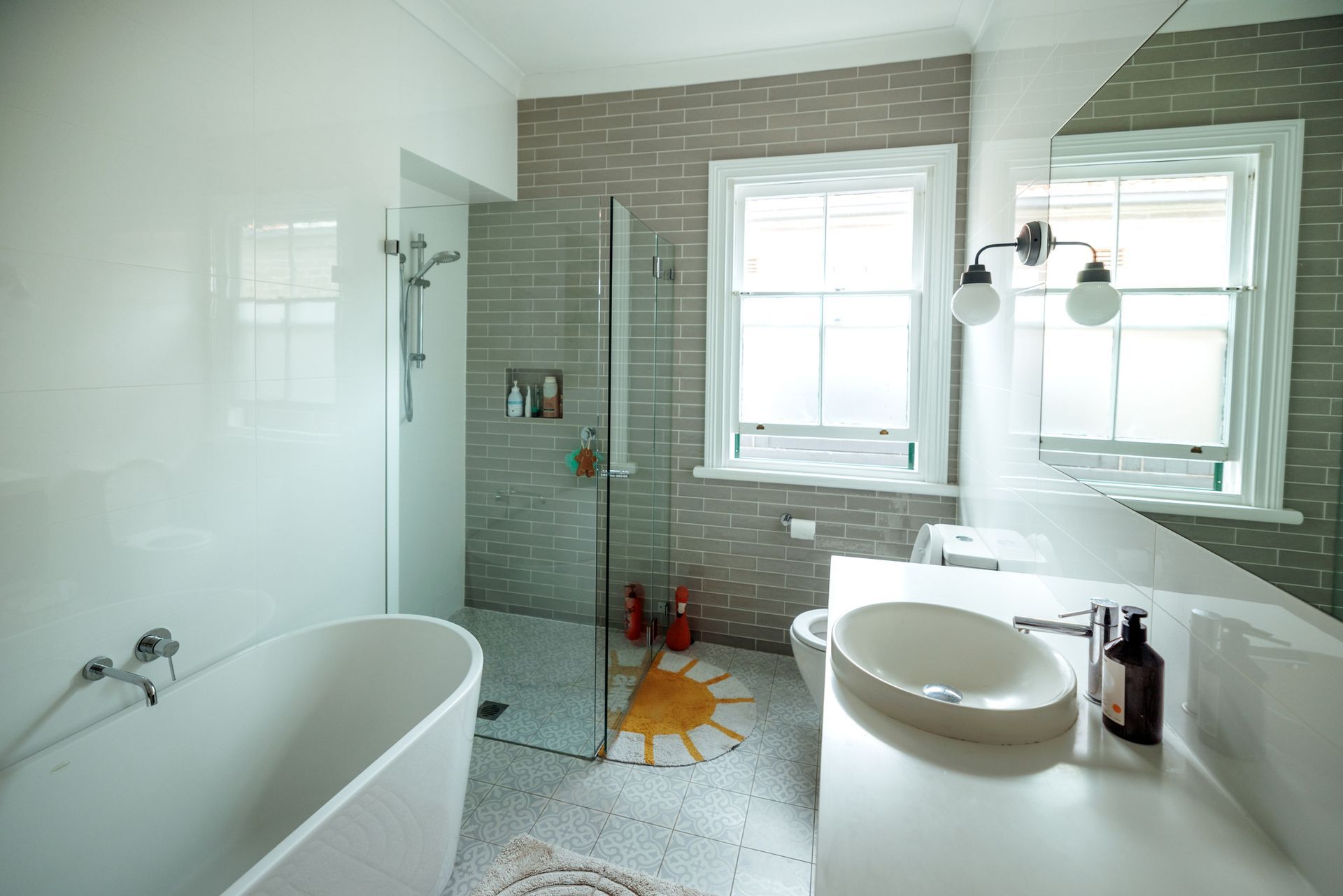 Bright modern bathroom with tub, glass shower, white sink, and tiled accent wall