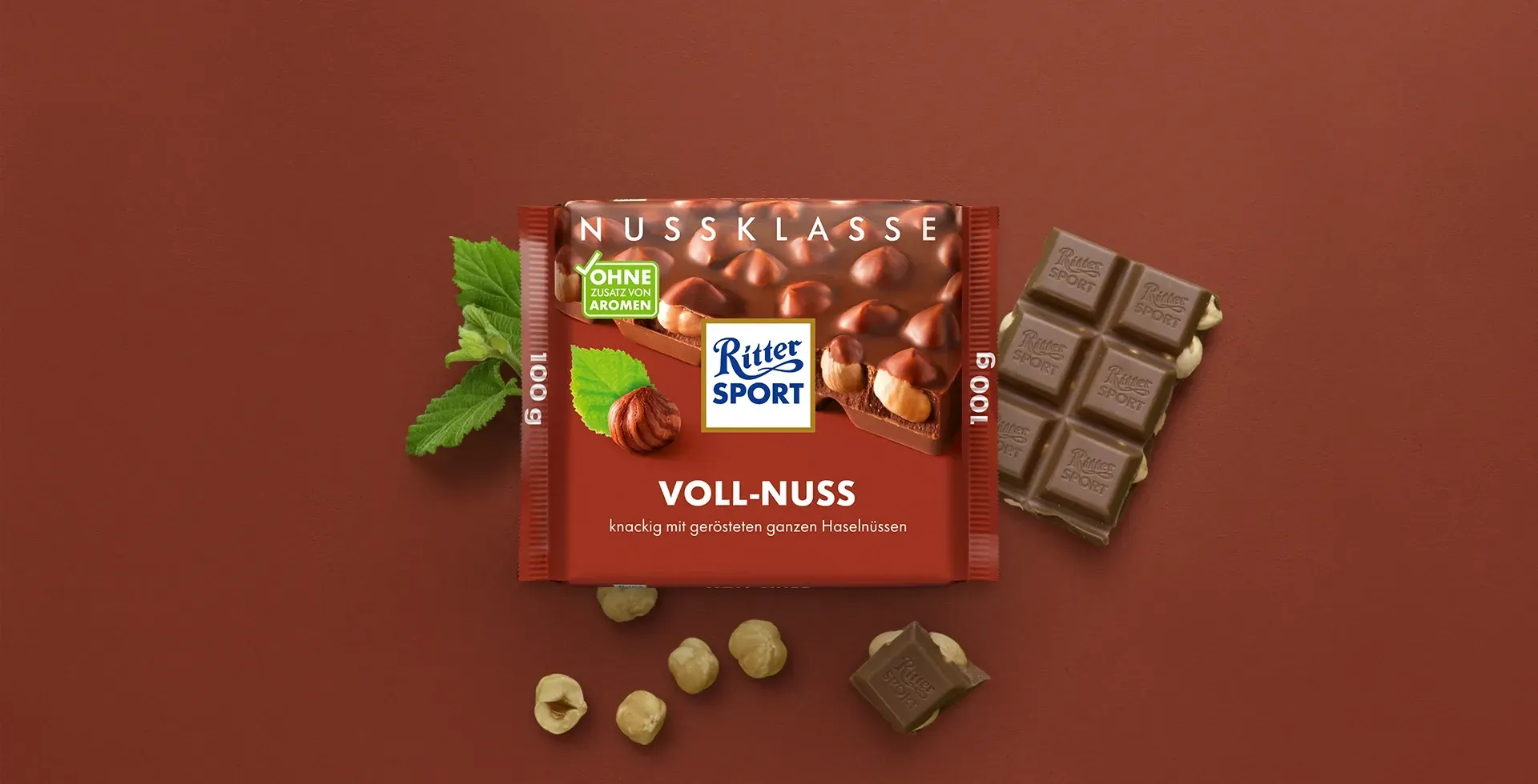 Verpackung einer blauen Schokoladentafel mit Nüssen, Schokoladenstückchen und dem Hinweis „55 % Kakaoanteil“ auf blauem Hintergrund