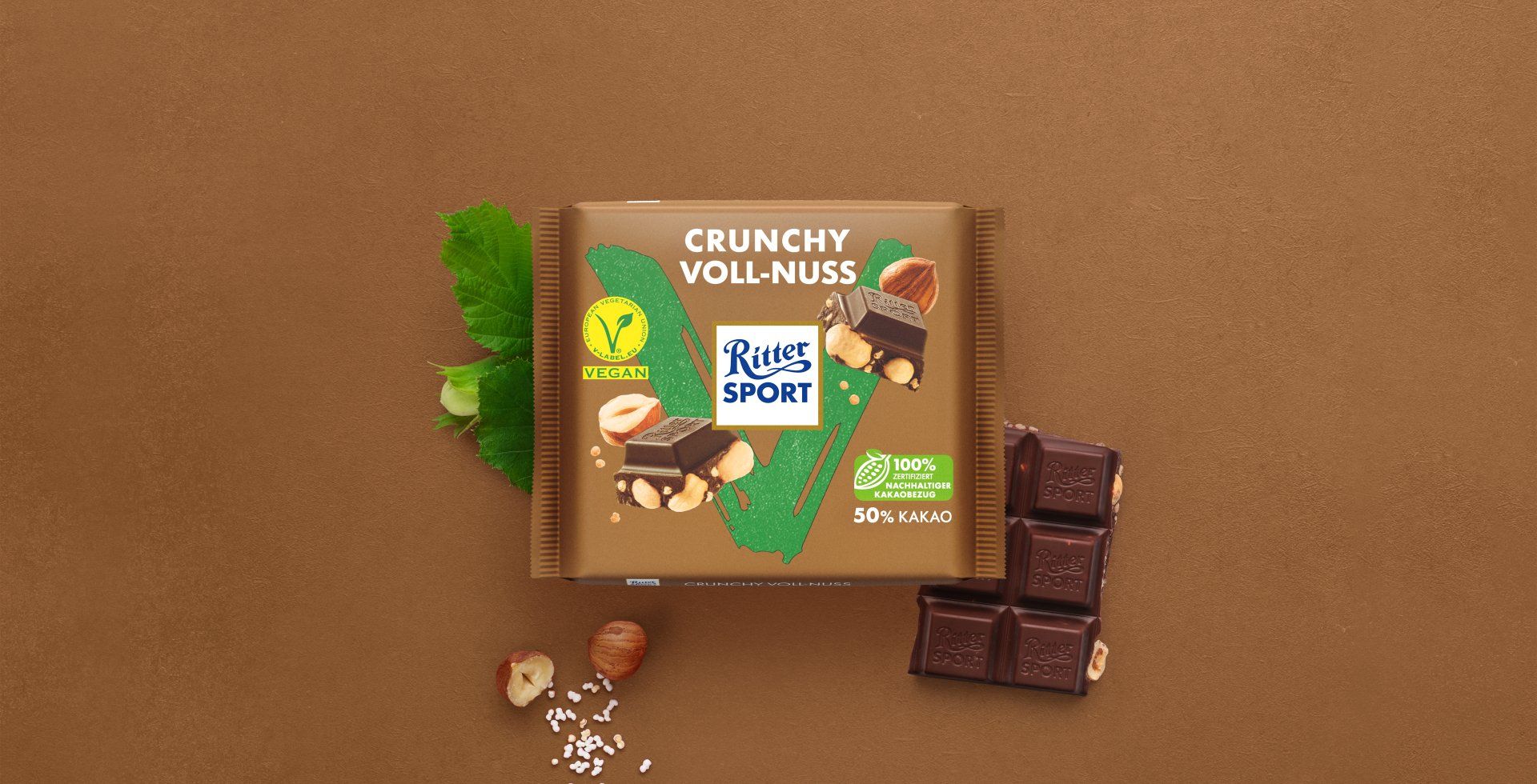 Verpackung einer blauen Schokoladentafel mit Nüssen, Schokoladenstückchen und dem Hinweis „55 % Kakaoanteil“ auf blauem Hintergrund