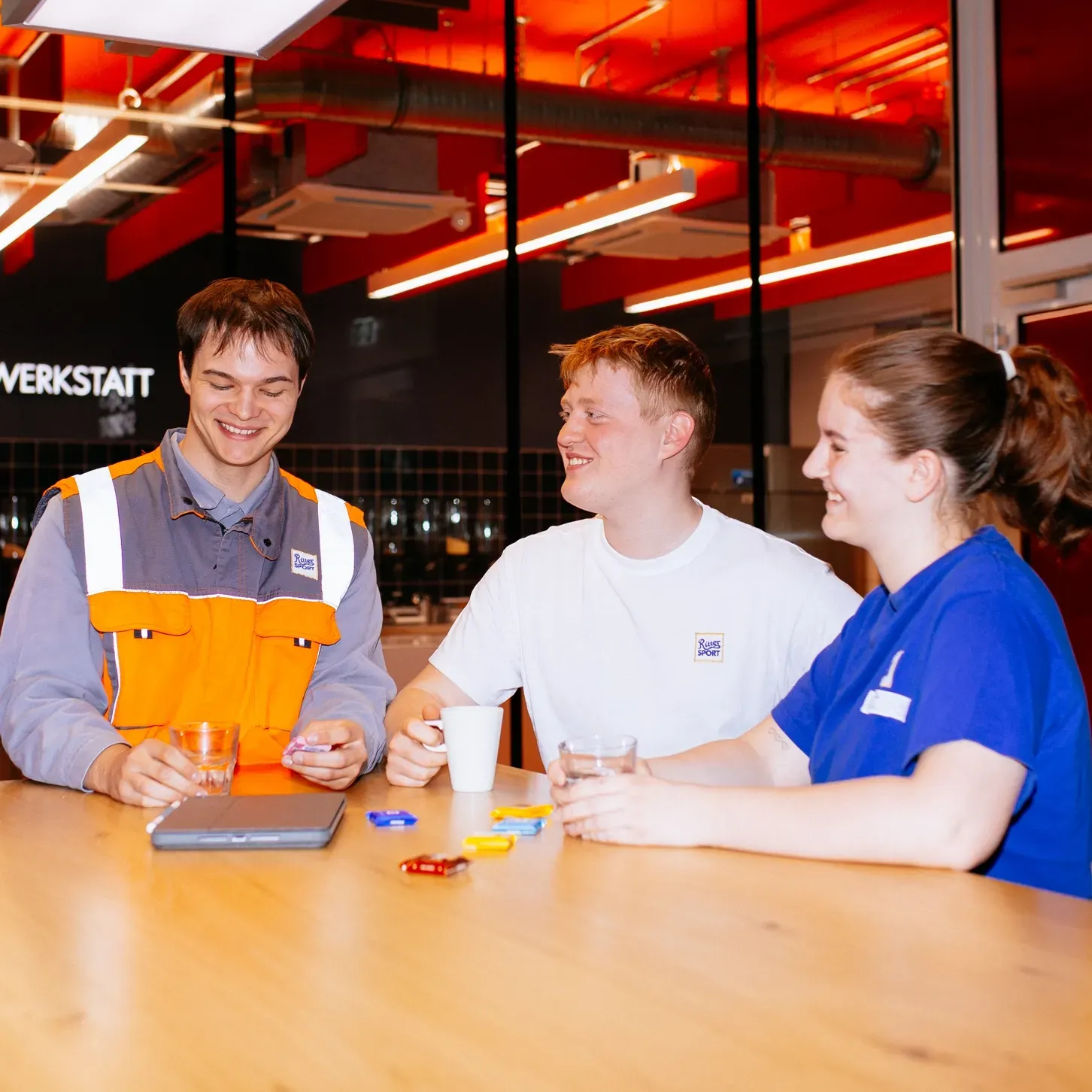 Three people are sitting at a table in front of a sign that says werkstatt