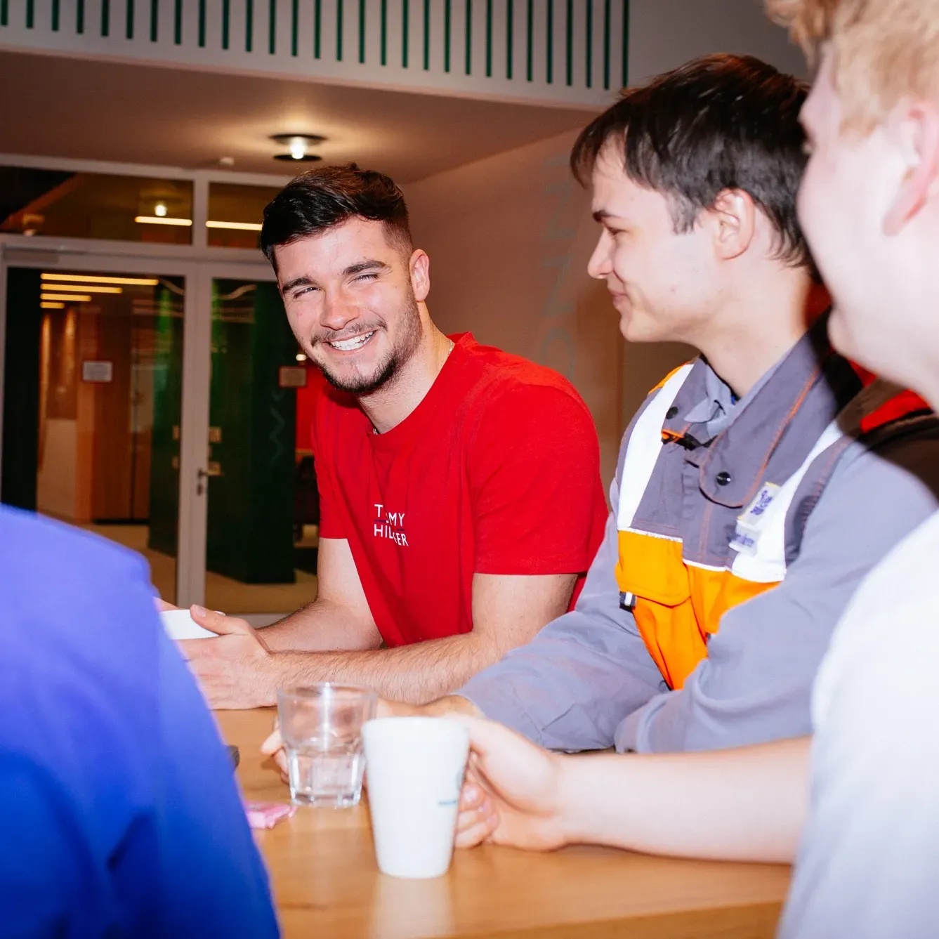 A man in a red shirt is sitting at a table with other men