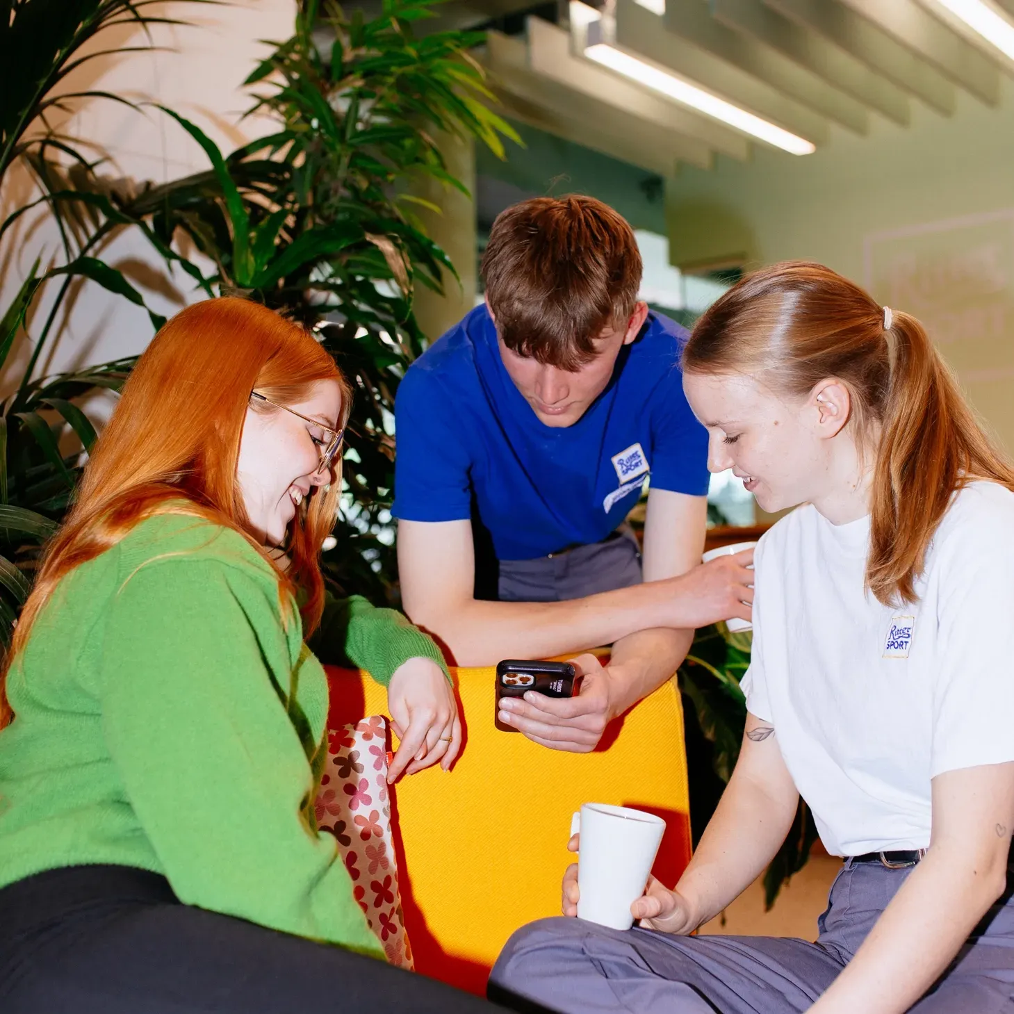 A group of young people are sitting around a table looking at a cell phone