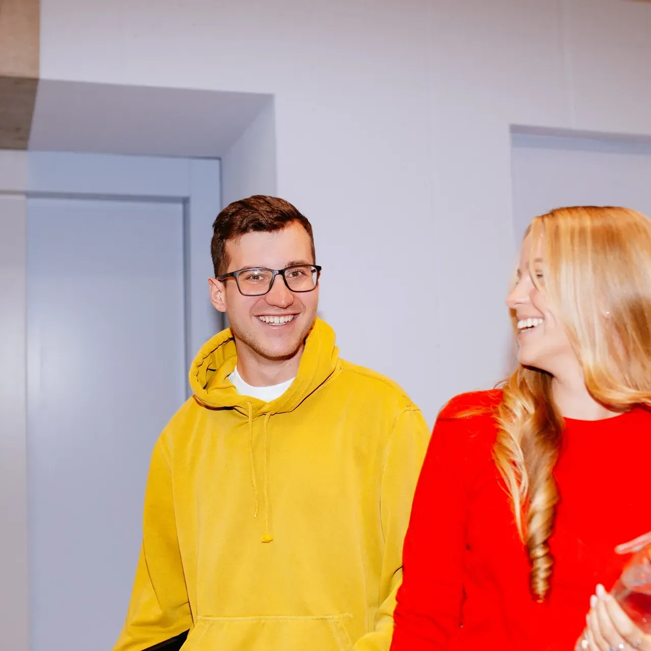 A man in a yellow hoodie stands next to a woman in a red sweater
