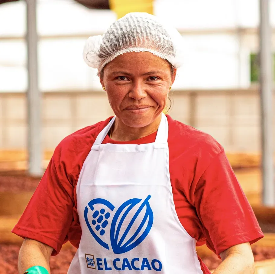 A woman wearing a red shirt and an apron that says el Cacao