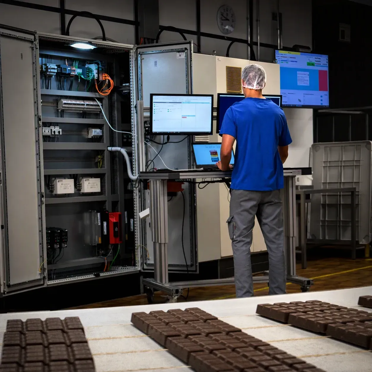 Ein Techniker in blauem Hemd arbeitet an einem Computer neben einer geöffneten Industriemaschine in einem Labor- oder Fabrikraum