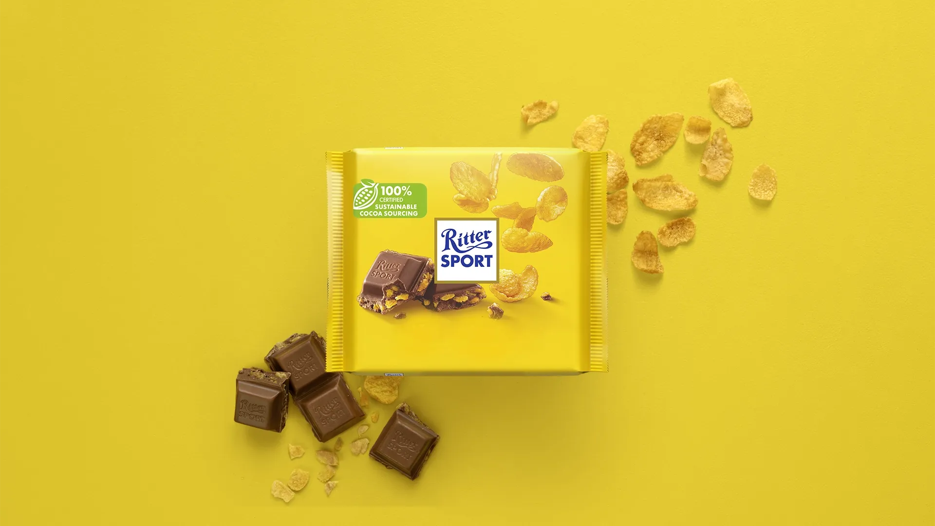 Ritter Sport chocolate bar packaging with cocoa beans, broken chocolate, and milk on a blue background.