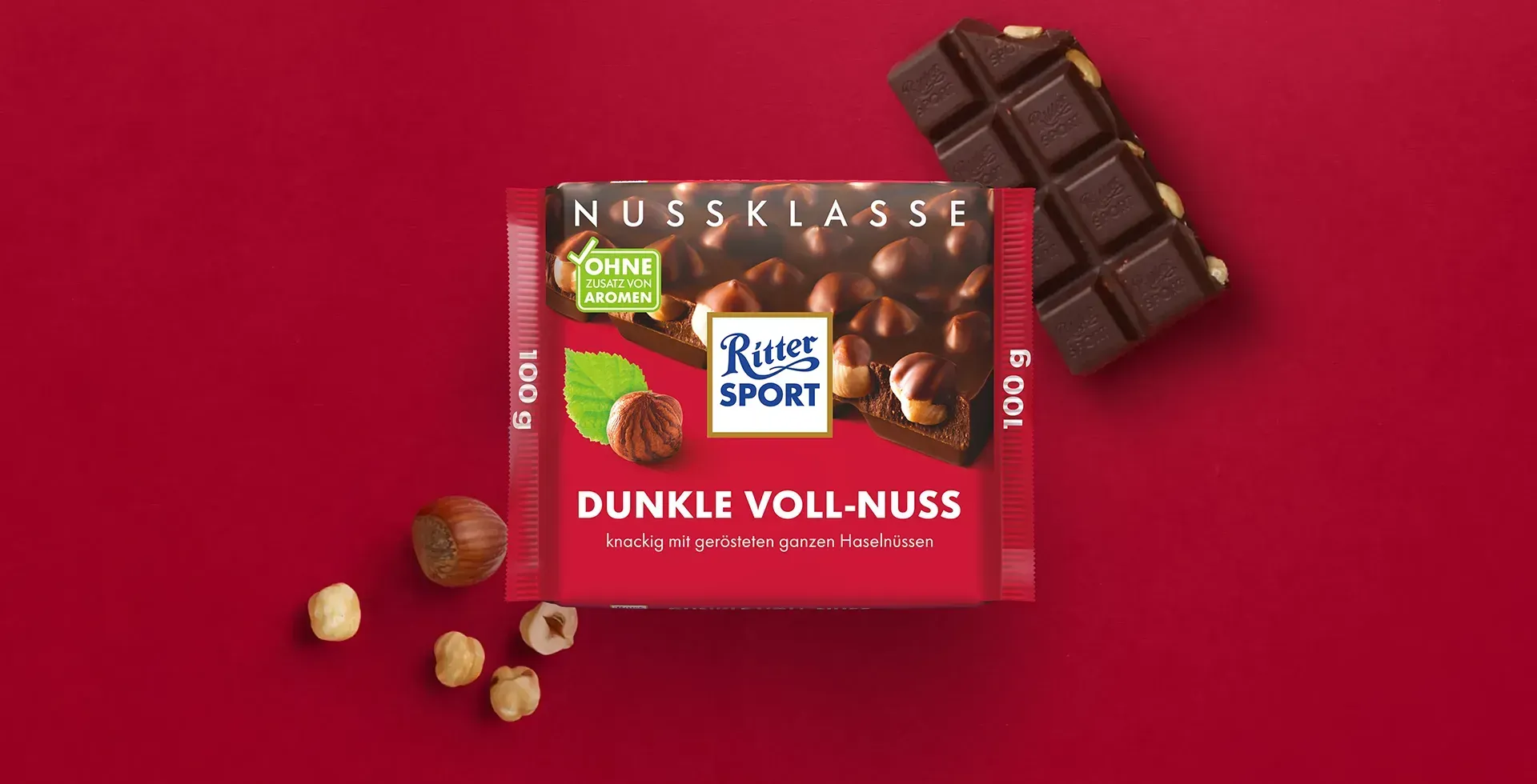 Verpackung einer blauen Schokoladentafel mit Nüssen, Schokoladenstückchen und dem Hinweis „55 % Kakaoanteil“ auf blauem Hintergrund