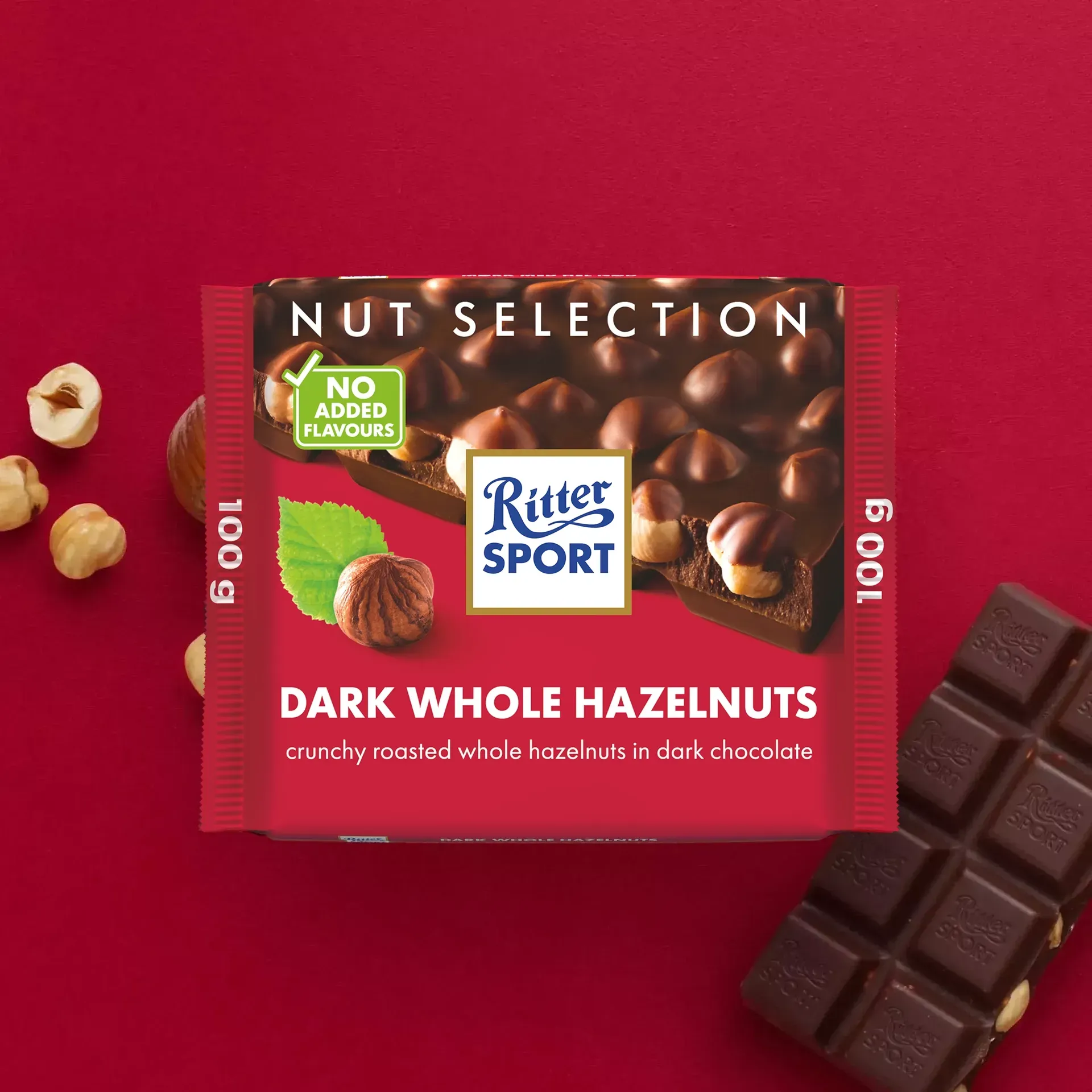 Ritter Sport dark chocolate bar with whole hazelnuts on a red background with loose nuts and broken pieces.