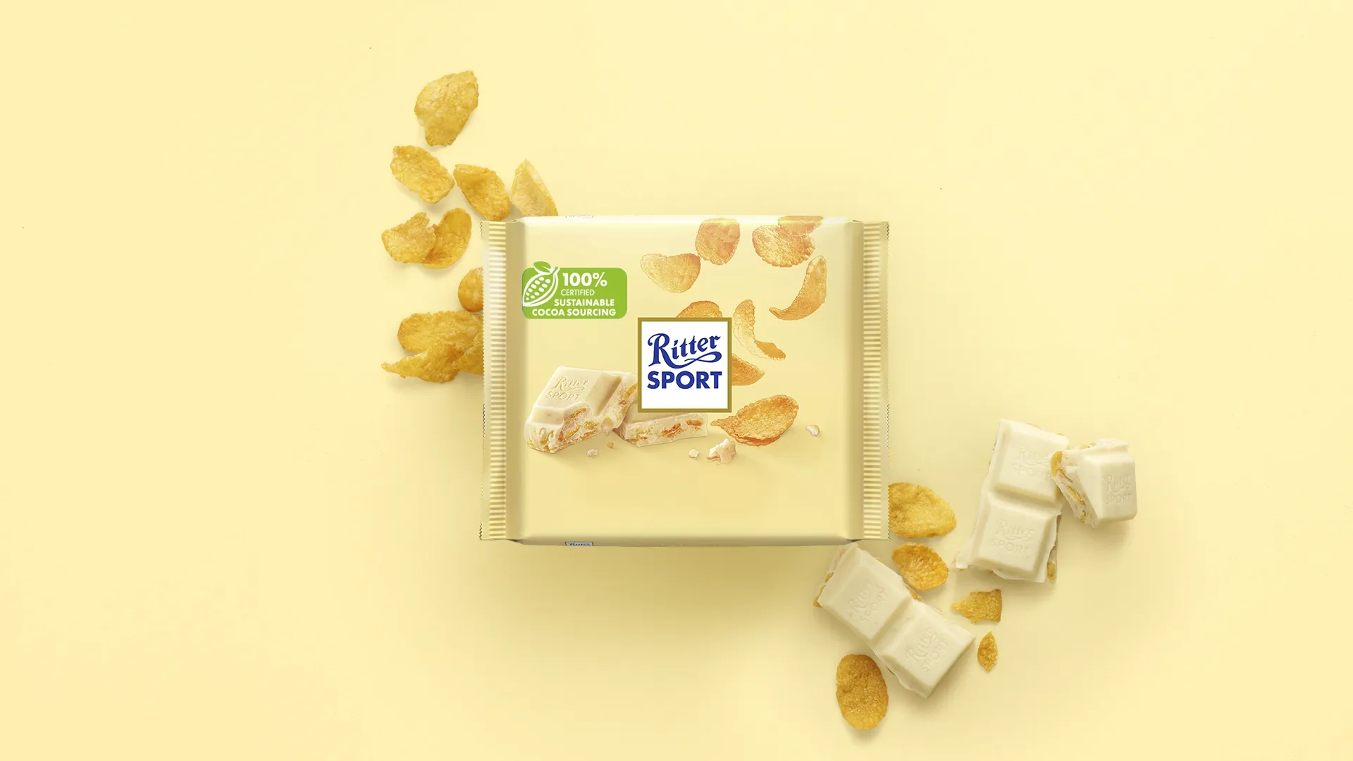 Ritter Sport chocolate bar packaging with cocoa beans, broken chocolate, and milk on a blue background.
