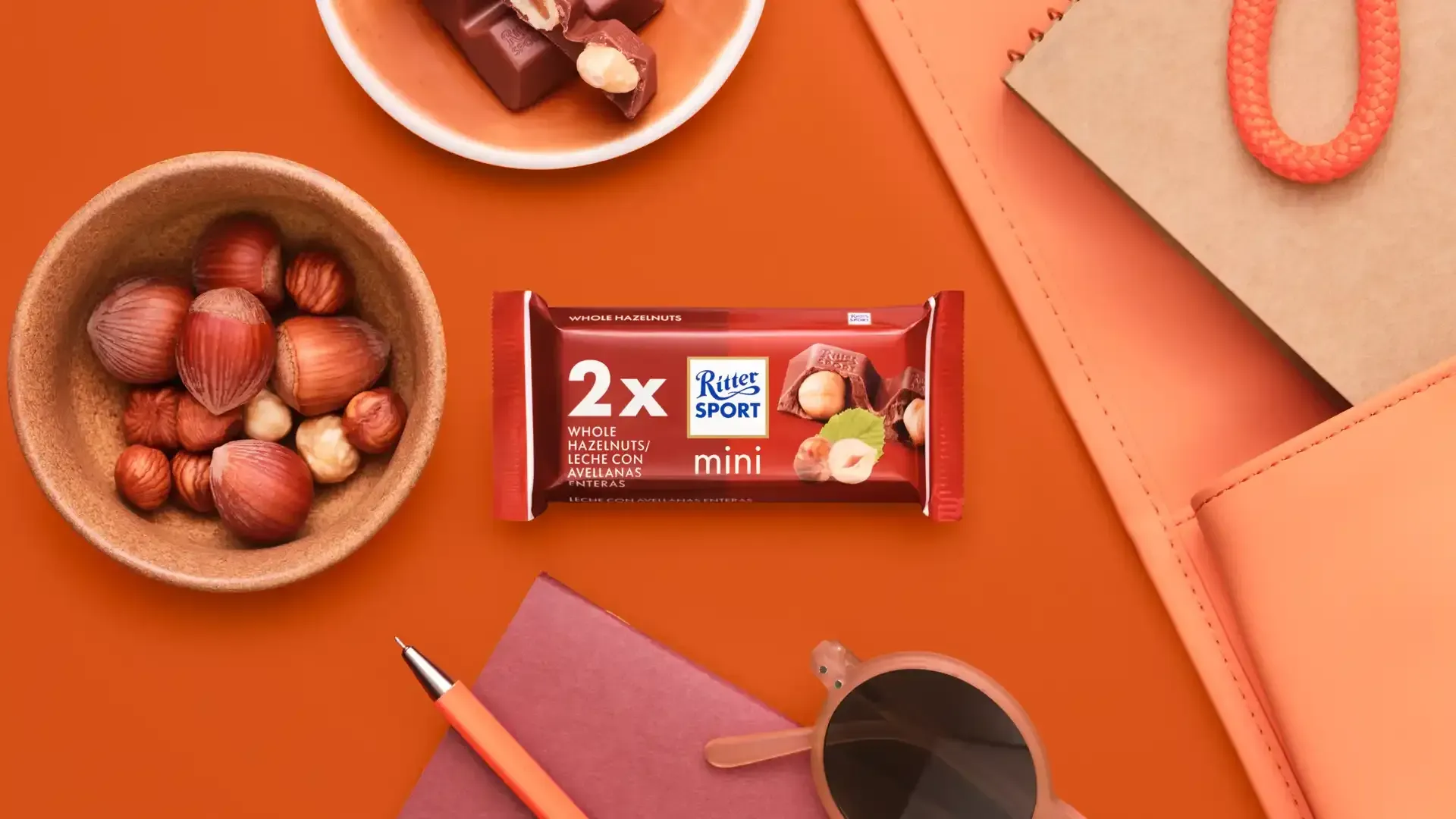 Ritter Sport chocolate bar packaging with cocoa beans, broken chocolate, and milk on a blue background.