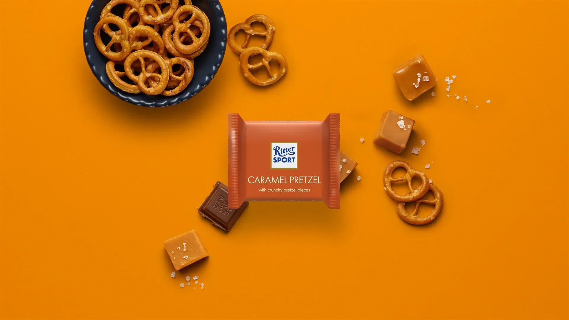 Ritter Sport chocolate bar packaging with cocoa beans, broken chocolate, and milk on a blue background.