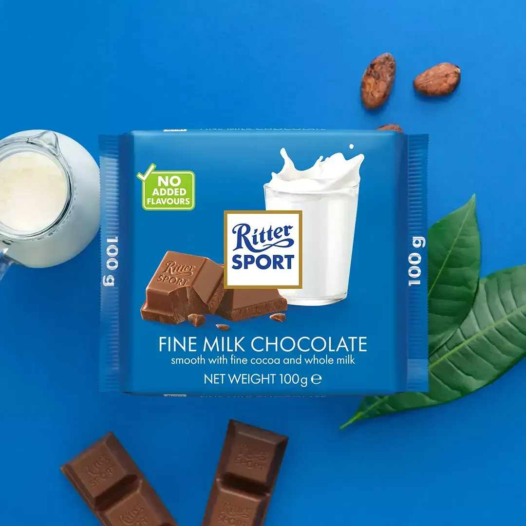 Ritter Sport milk chocolate bar with milk splash graphic, cocoa beans, milk jug, and blue background.