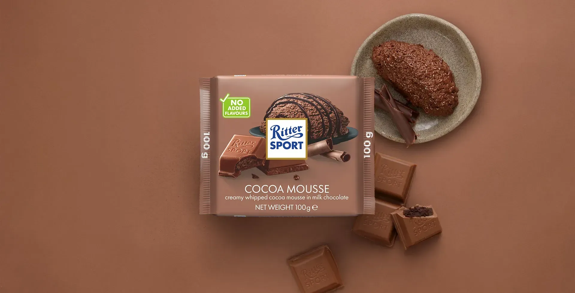 Ritter Sport chocolate bar packaging with cocoa beans, broken chocolate, and milk on a blue background.