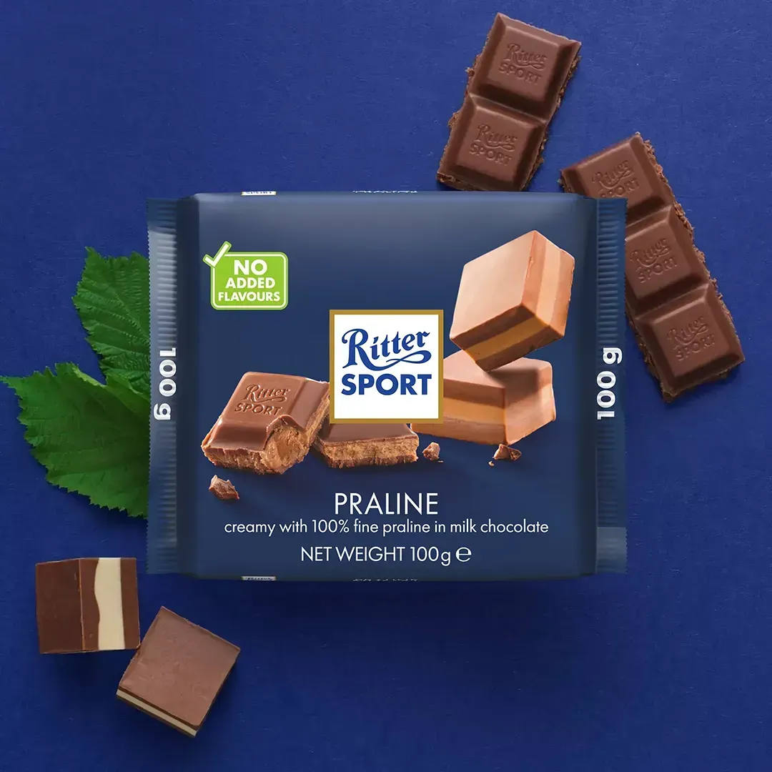 Ritter Sport chocolate bar with hazelnut filling on blue background, with detached chocolate squares and a leaf.
