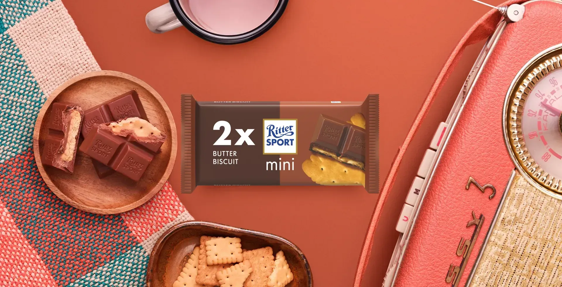 Ritter Sport chocolate bar packaging with cocoa beans, broken chocolate, and milk on a blue background.