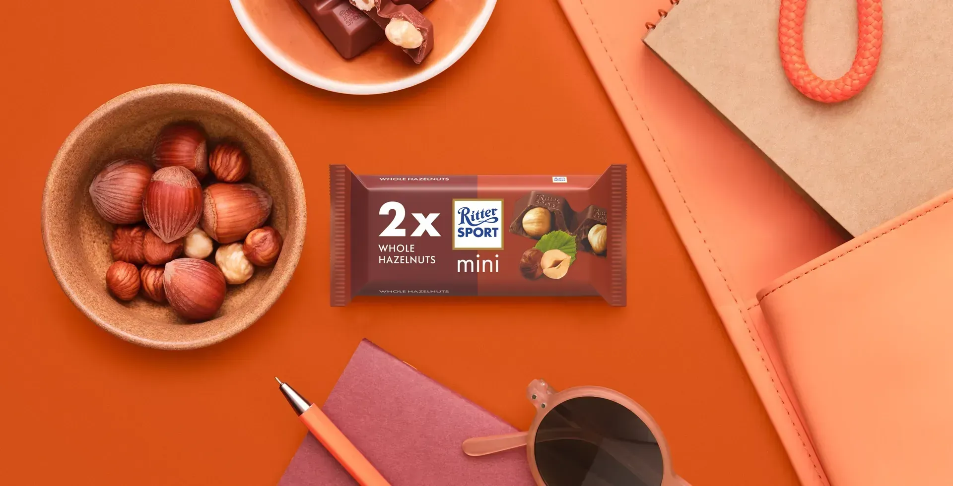 Ritter Sport chocolate bar packaging with cocoa beans, broken chocolate, and milk on a blue background.
