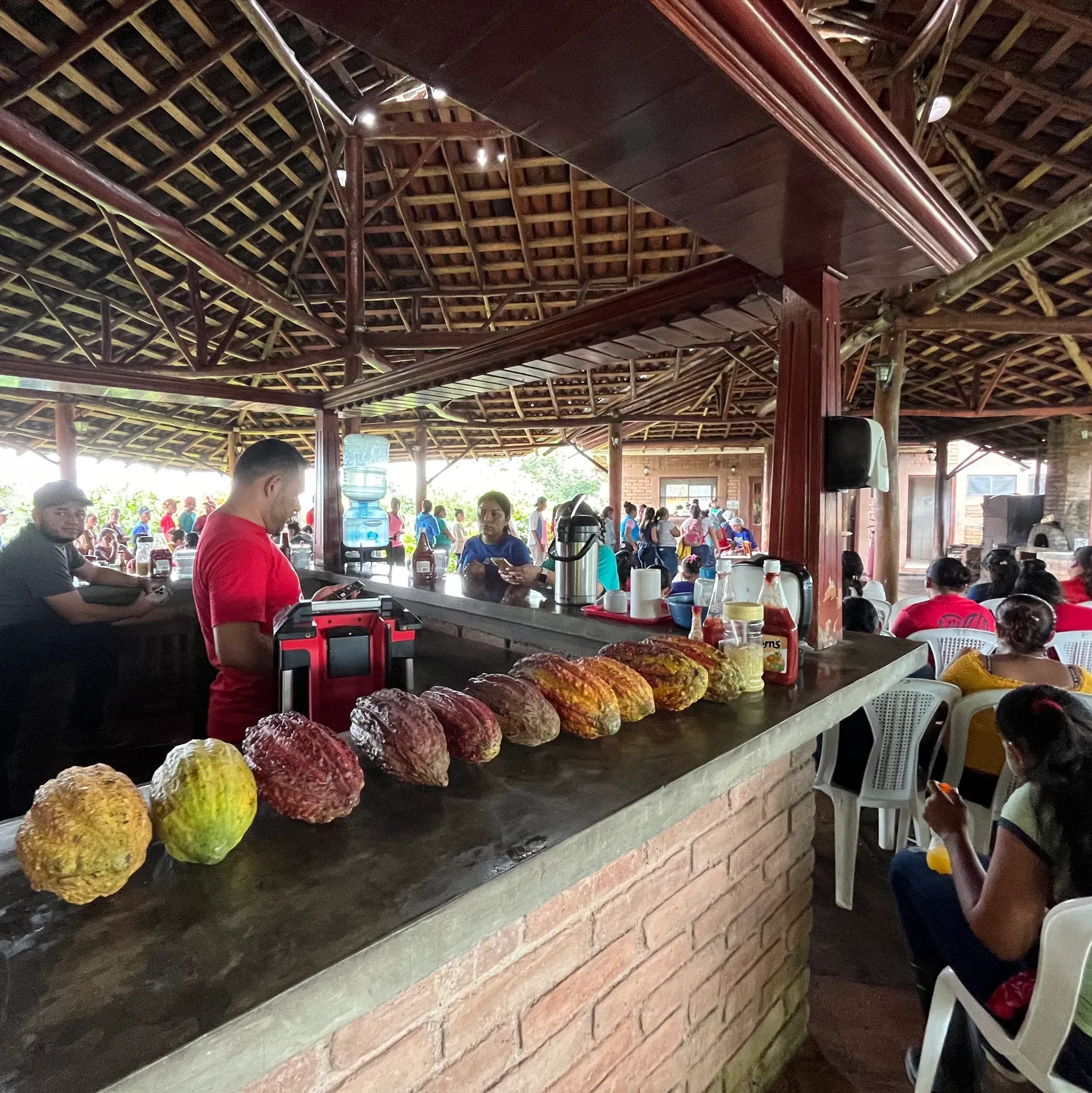 A man in a red shirt is standing behind a counter filled with food.