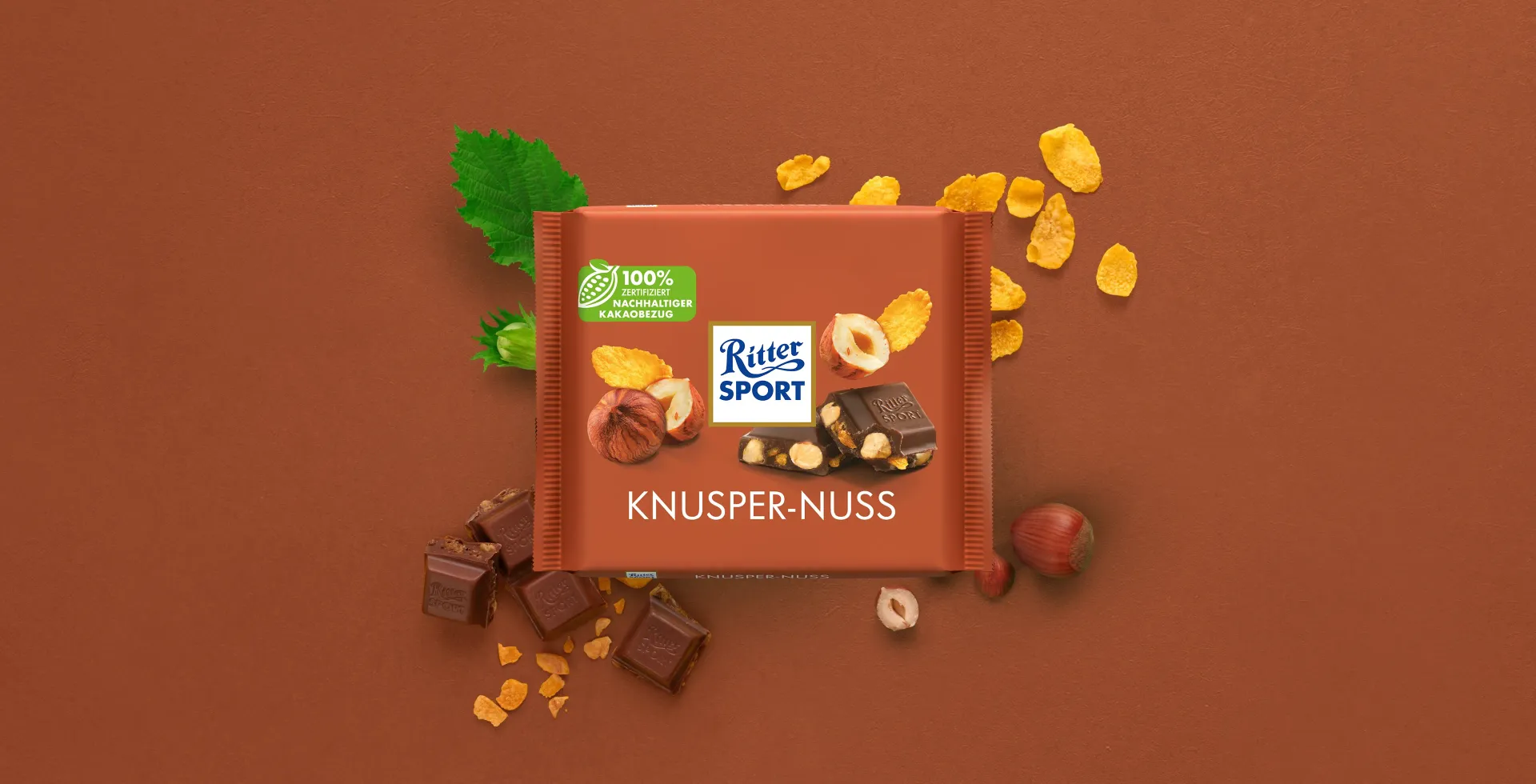 Verpackung einer blauen Schokoladentafel mit Nüssen, Schokoladenstückchen und dem Hinweis „55 % Kakaoanteil“ auf blauem Hintergrund