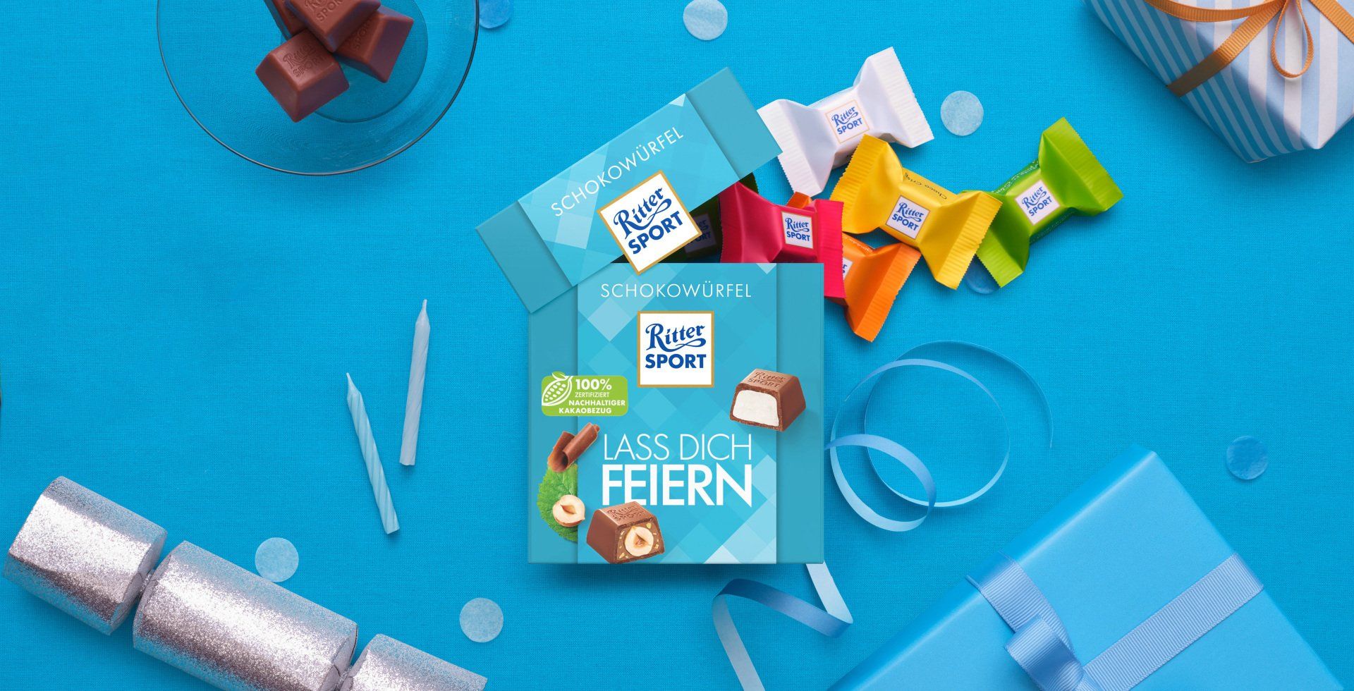 Verpackung einer blauen Schokoladentafel mit Nüssen, Schokoladenstückchen und dem Hinweis „55 % Kakaoanteil“ auf blauem Hintergrund