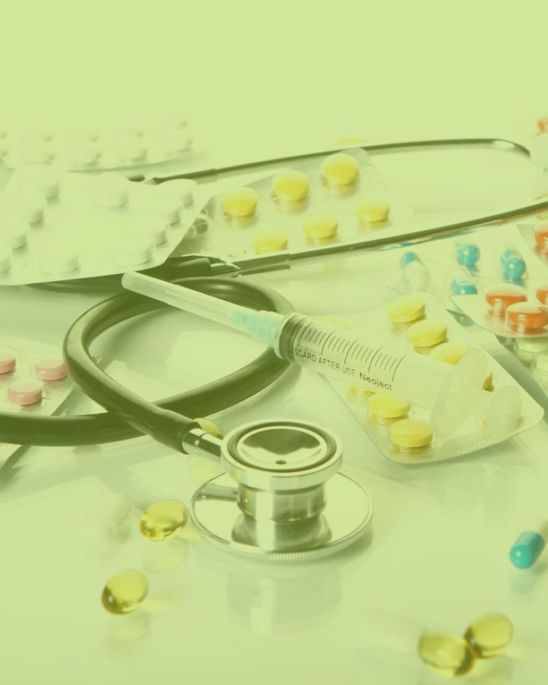 A stethoscope , syringe , pills and capsules are on a table.