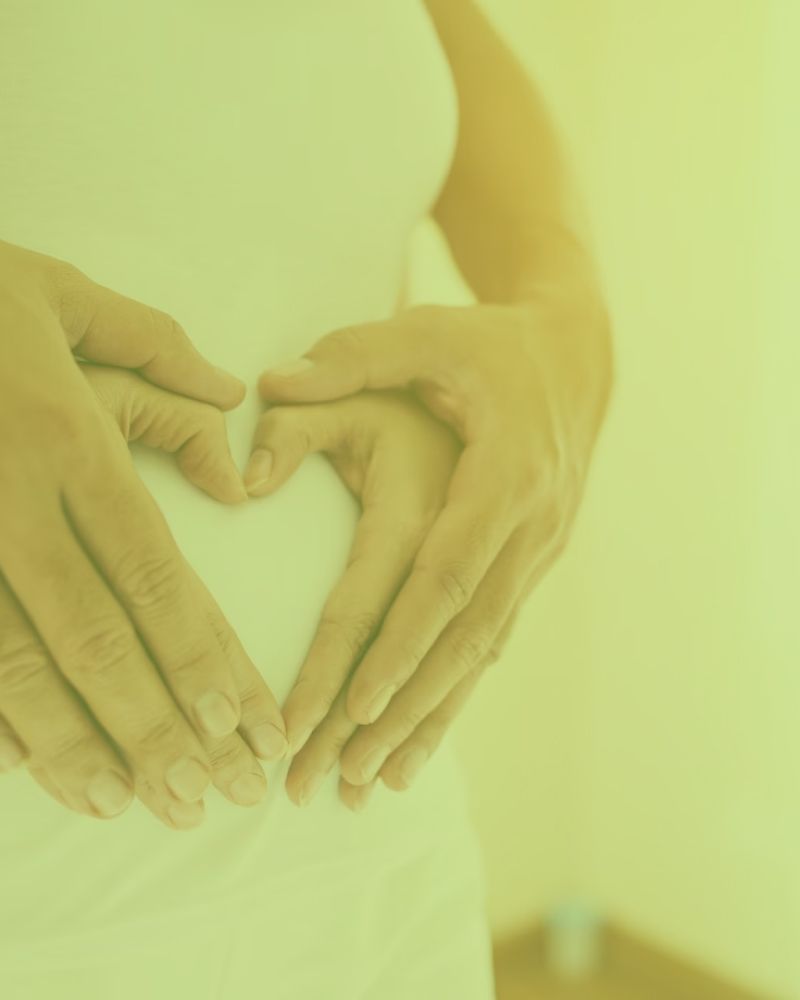 A pregnant woman is making a heart shape with her hands on her belly.