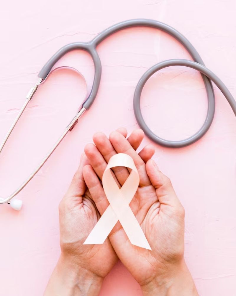 A person is holding a pink ribbon in their hands in front of a stethoscope.