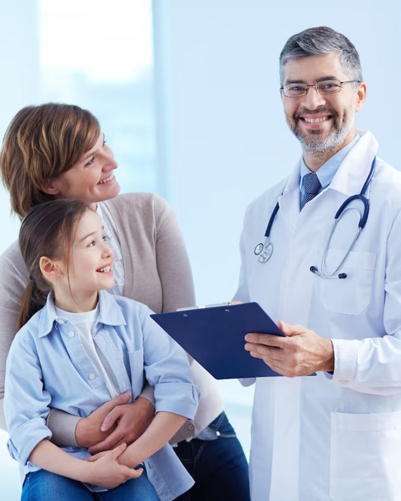 A doctor is holding a clipboard while a woman and child look on.