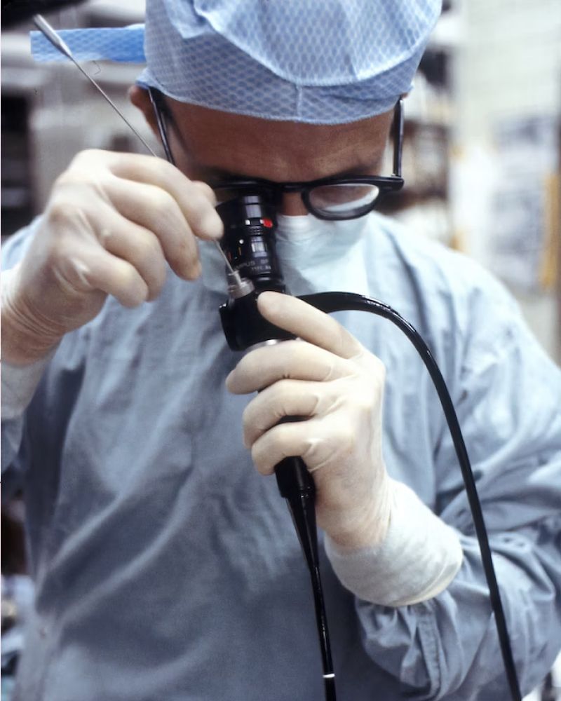 A surgeon wearing a surgical gown and gloves looks through a scope