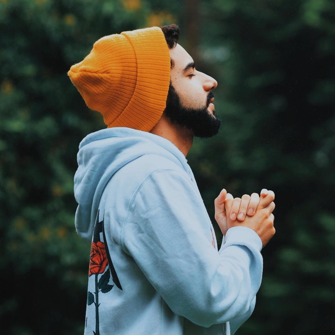 A man wearing a beanie and a hoodie is praying