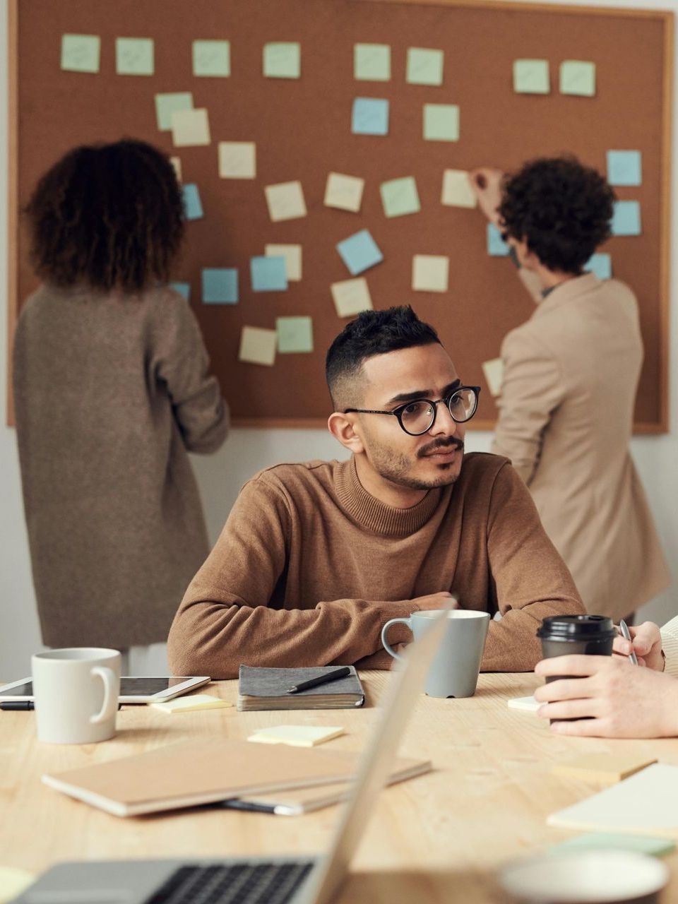 A man is sitting at a table in front of a board with sticky notes on it.