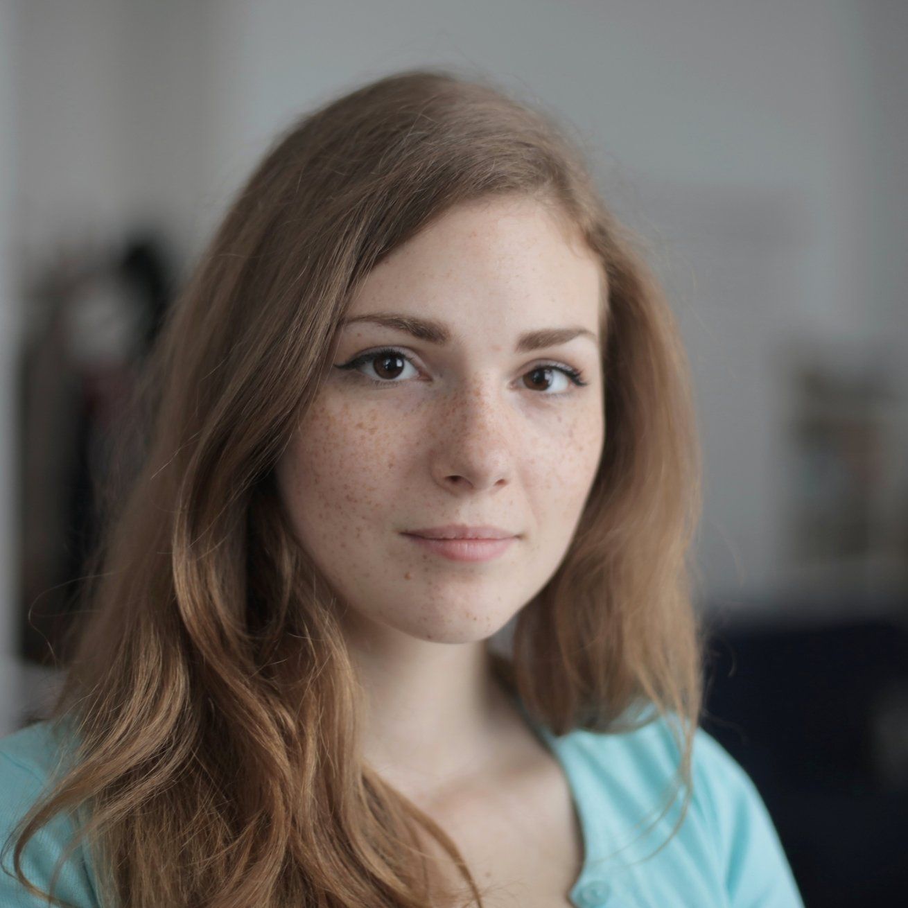 A woman with long brown hair and freckles is wearing a blue shirt and looking at the camera.