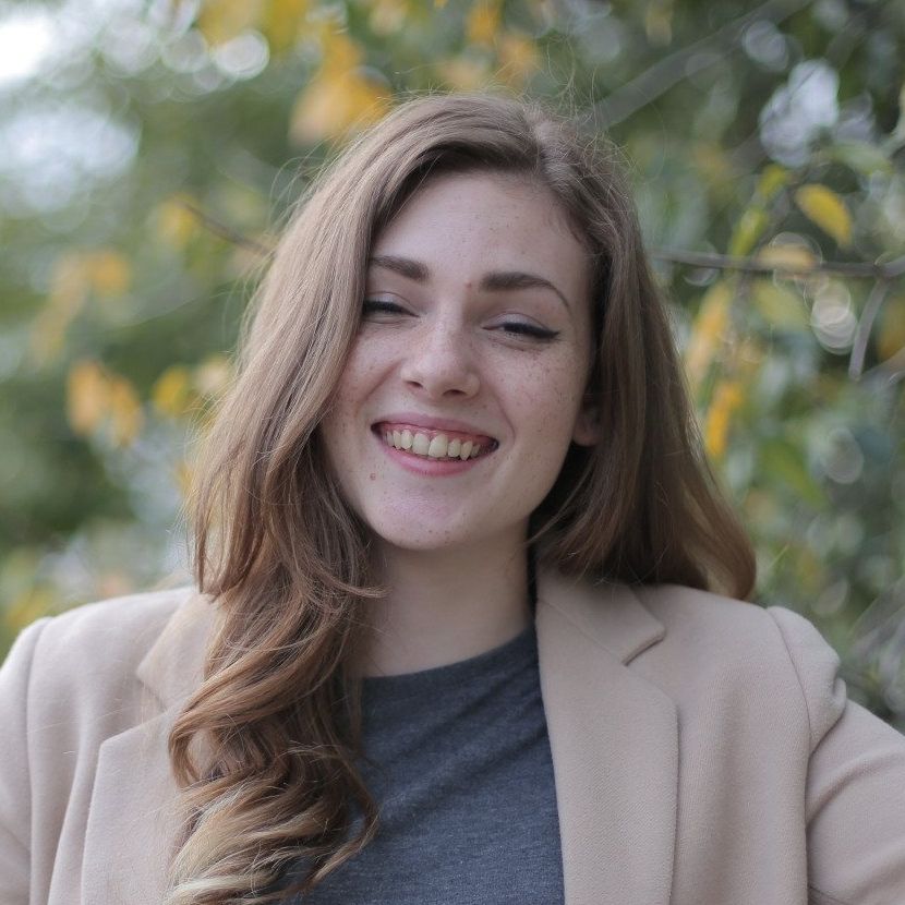 A woman in a tan jacket and gray shirt is smiling for the camera.