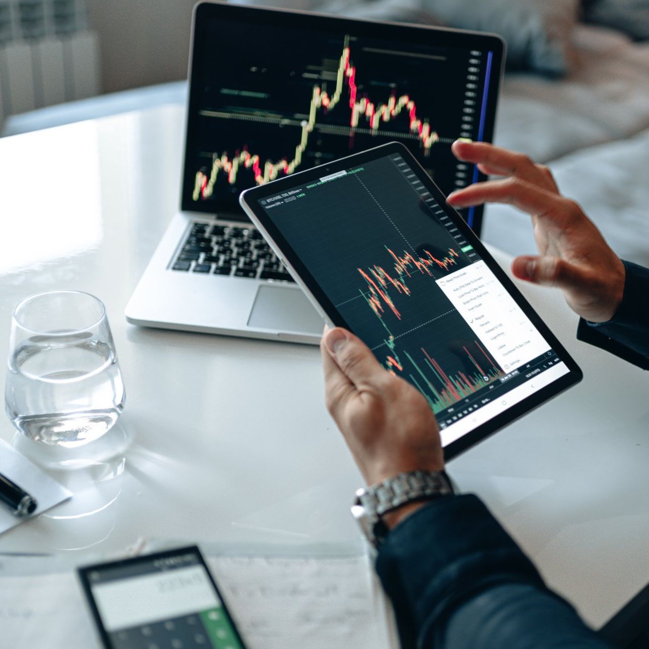 A person is holding a tablet with a graph on it in front of a laptop.