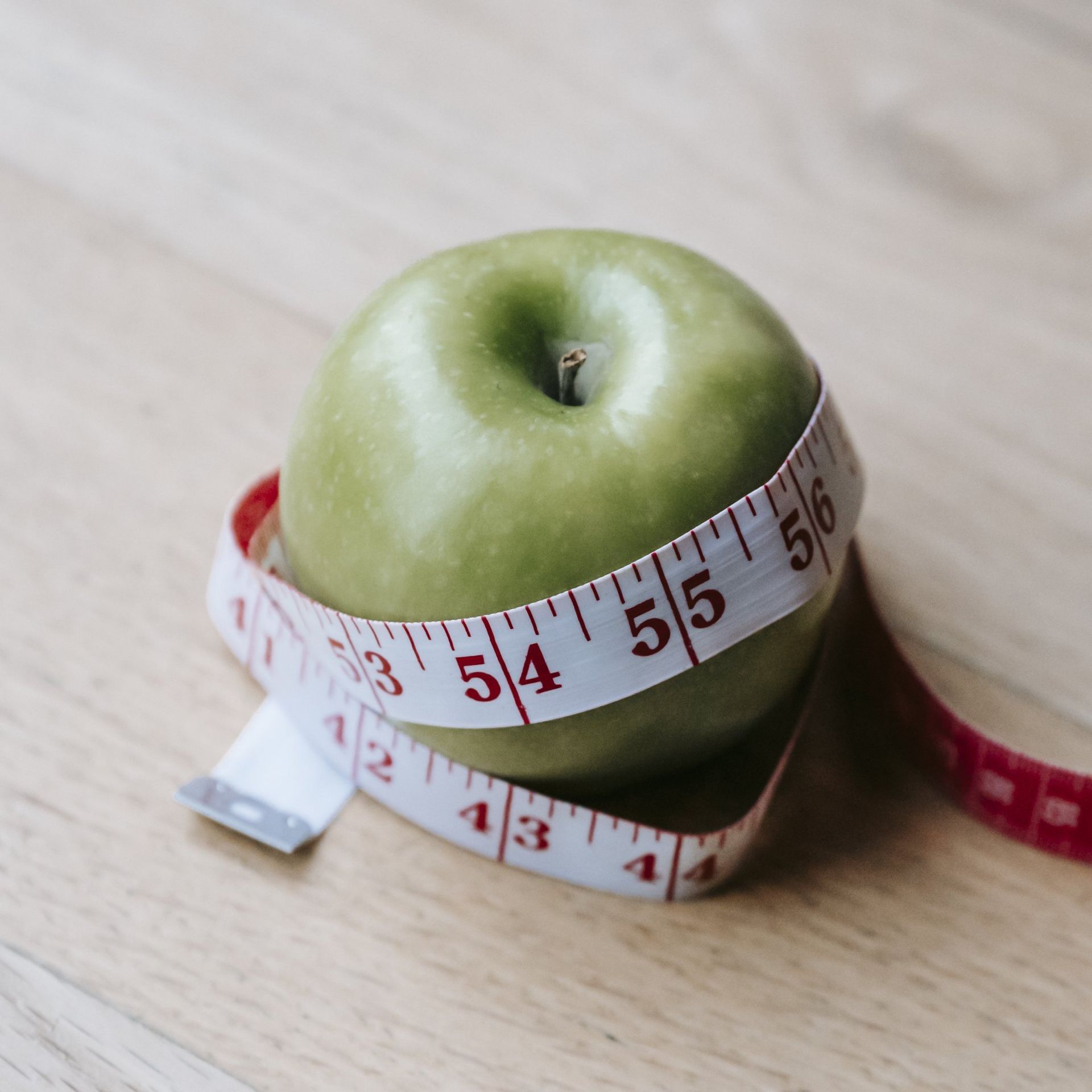 A green apple with a measuring tape wrapped around it