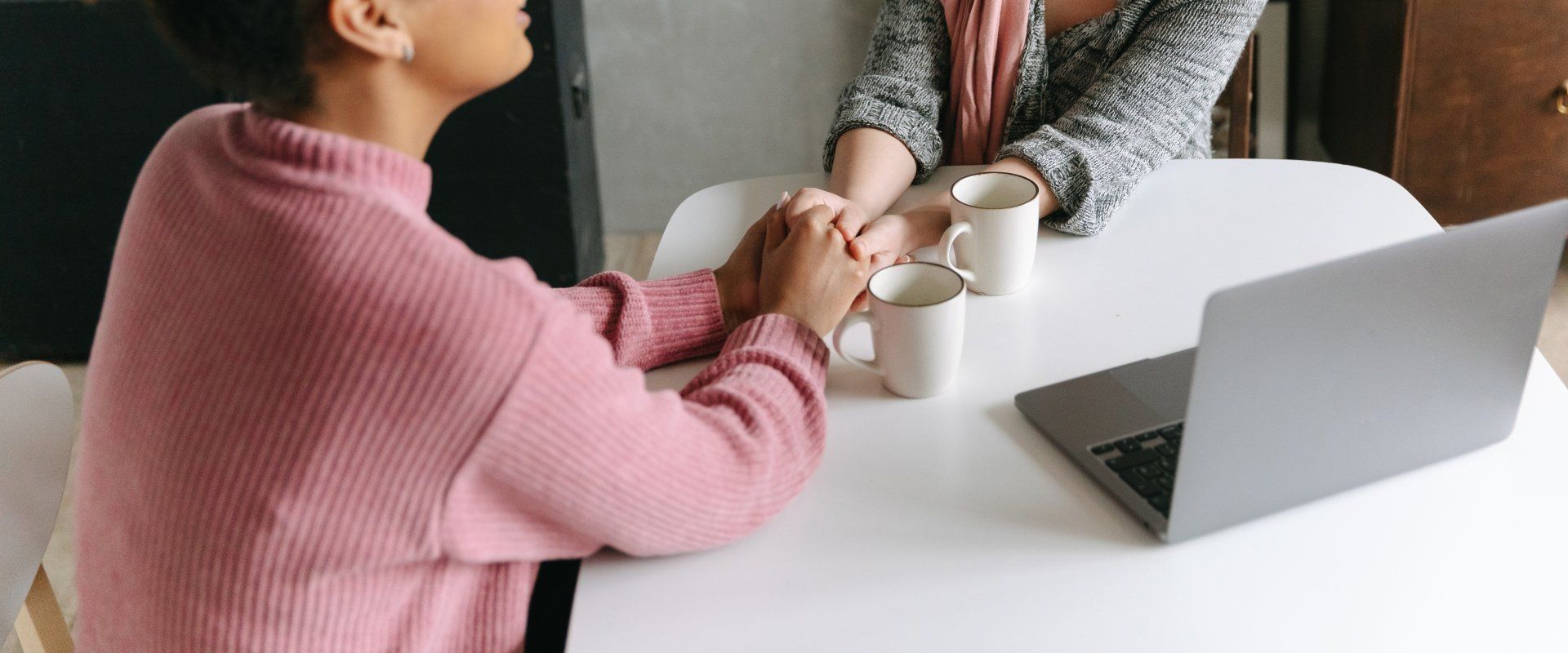 Two women are sitting at a table with cups of coffee and a laptop.