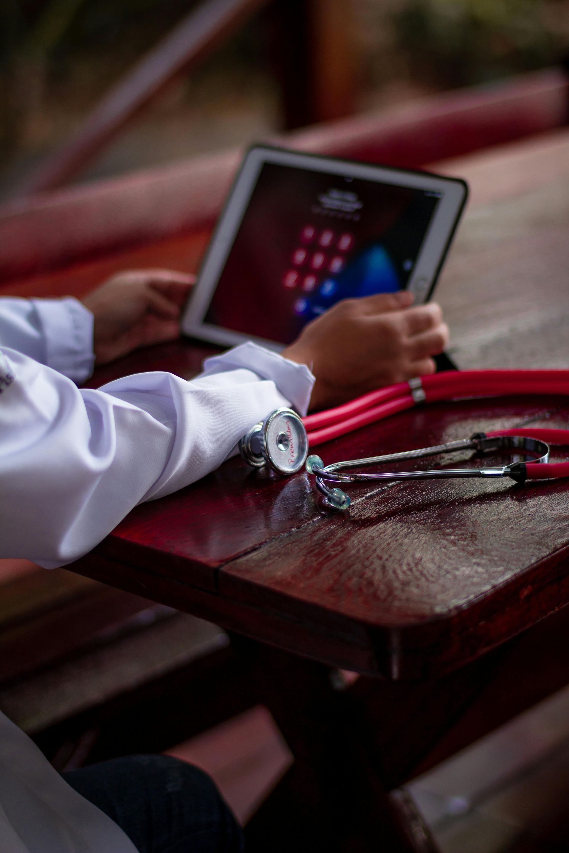 Person using a tablet on a table, with a stethoscope and notebook nearby