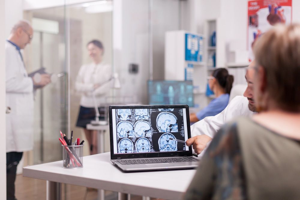 A woman is sitting at a table looking at an x-ray on a laptop computer.